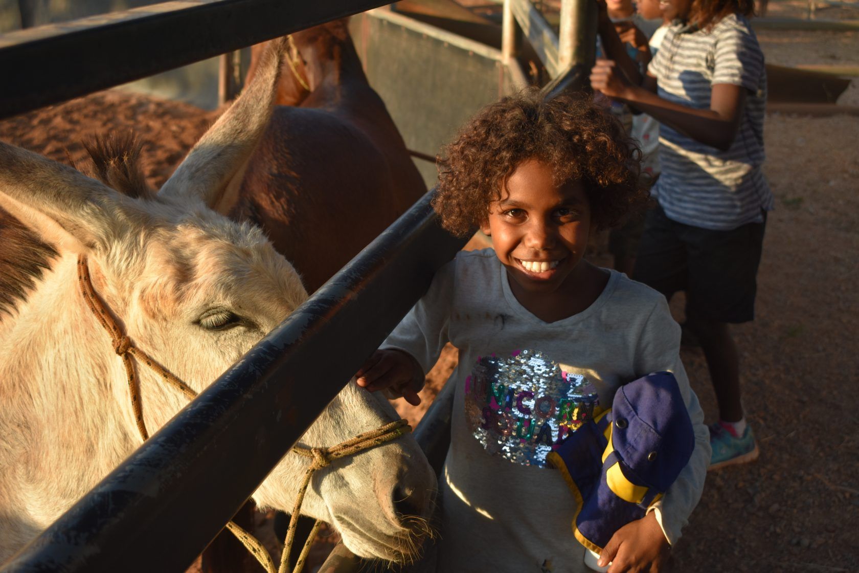 A little girl is standing next to a donkey behind a fence.
