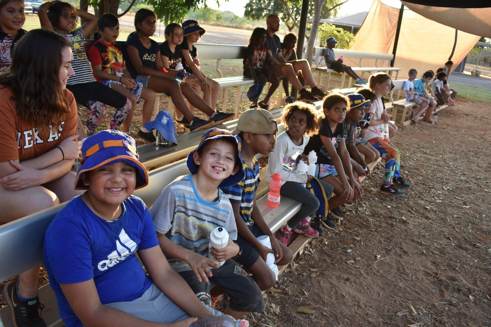 A group of children are sitting on a bench outside.