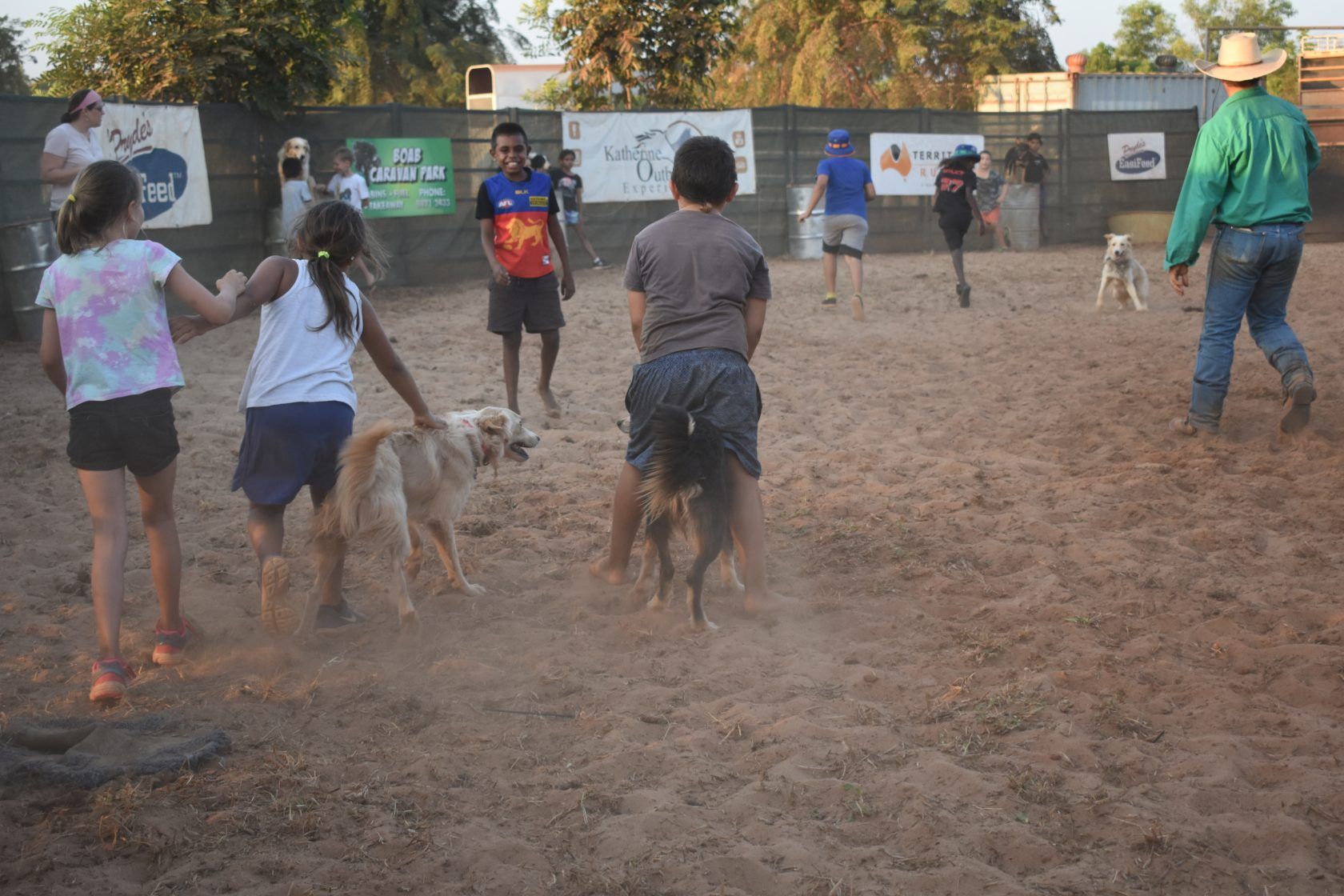 A group of people playing with dogs in a dirt field
