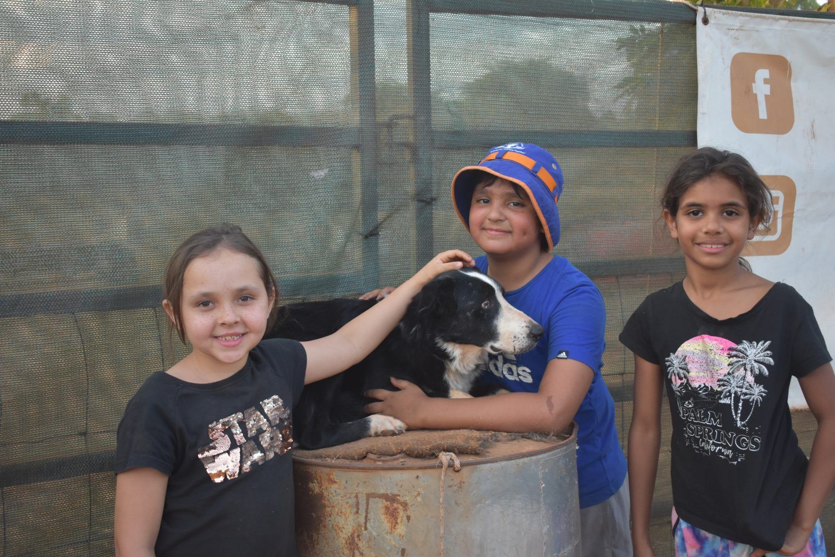 A boy and two girls are petting a black and white dog