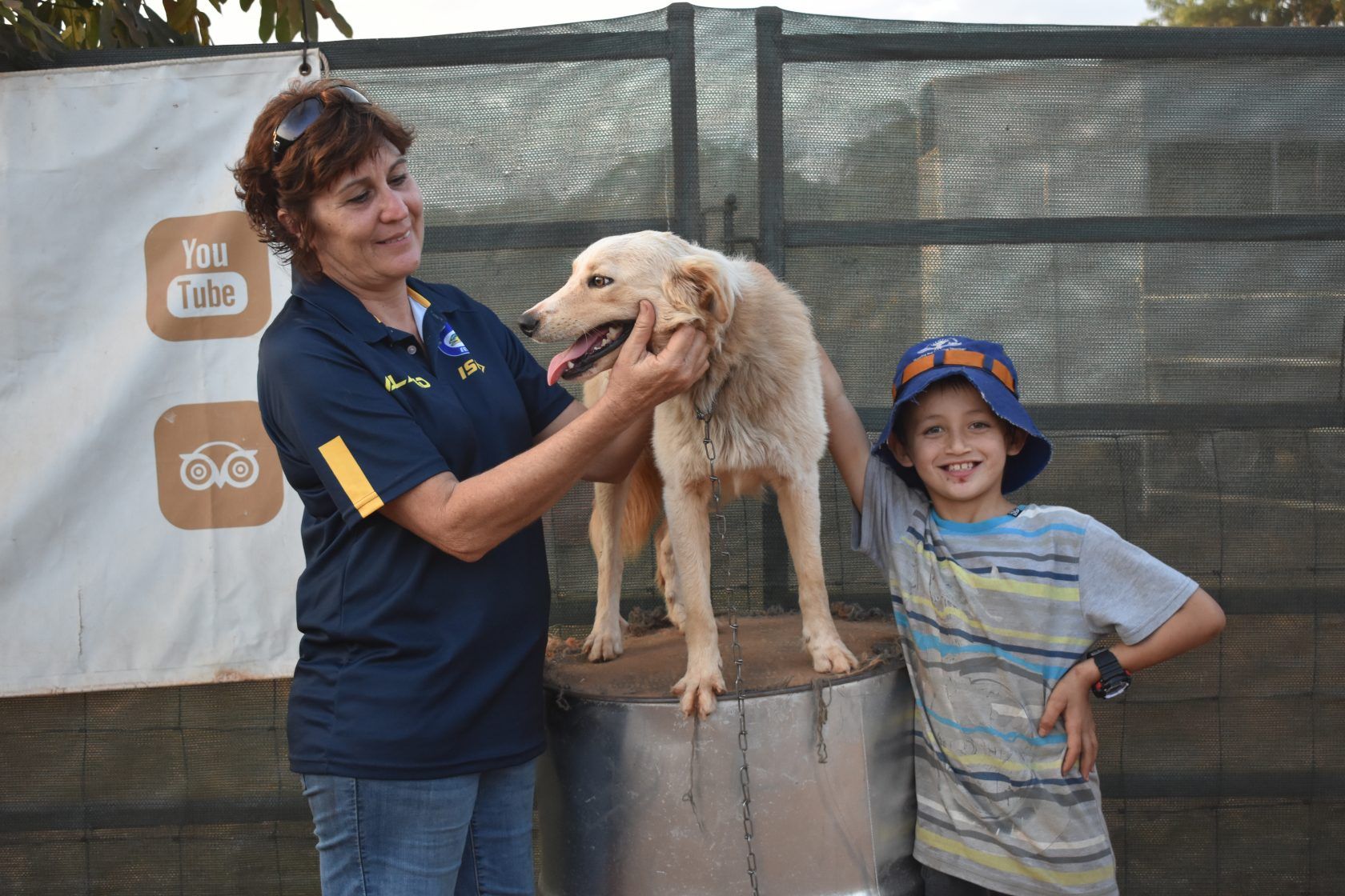 A woman and a boy are standing next to a dog on a barrel.