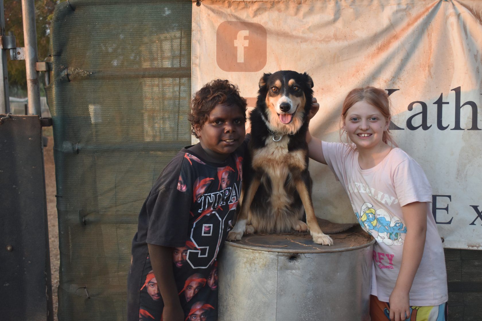 A boy and a girl are posing for a picture with a dog on a barrel.
