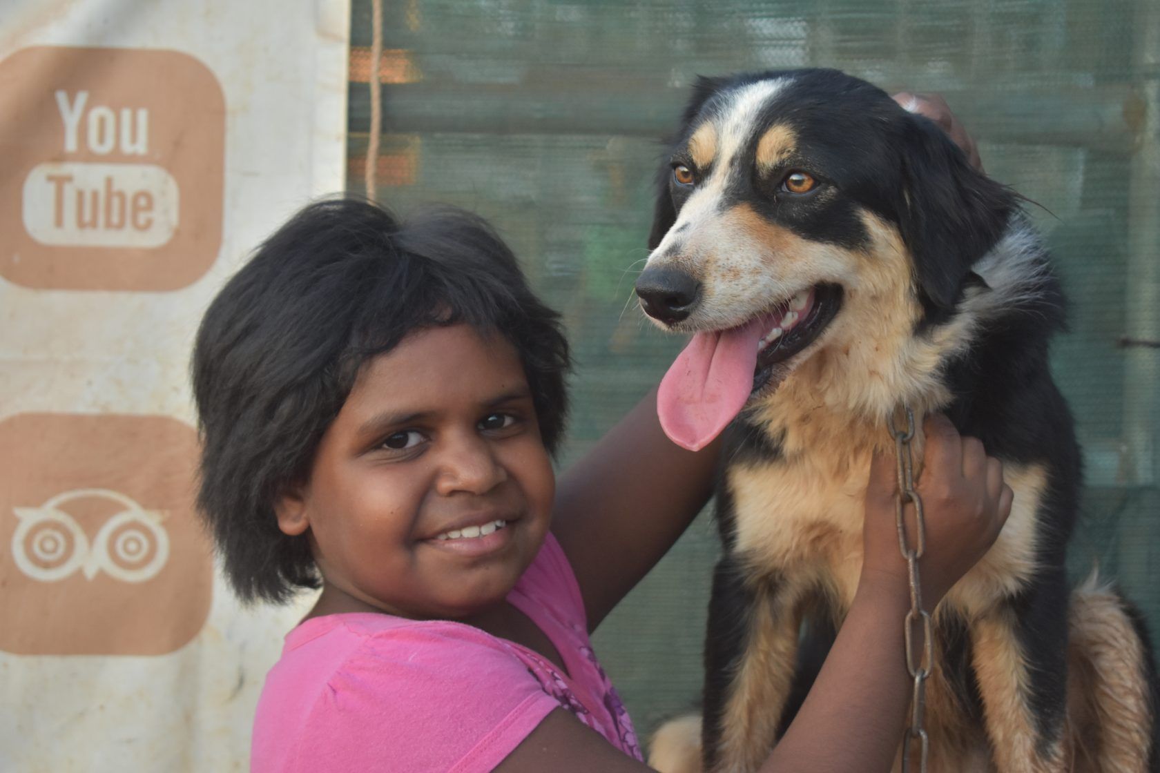 A little girl is holding a dog in front of a sign that says you tube