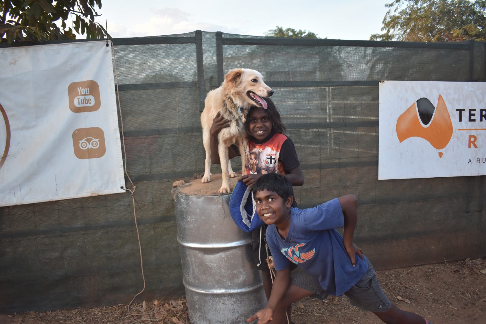 A boy and a dog are standing on top of a metal barrel.