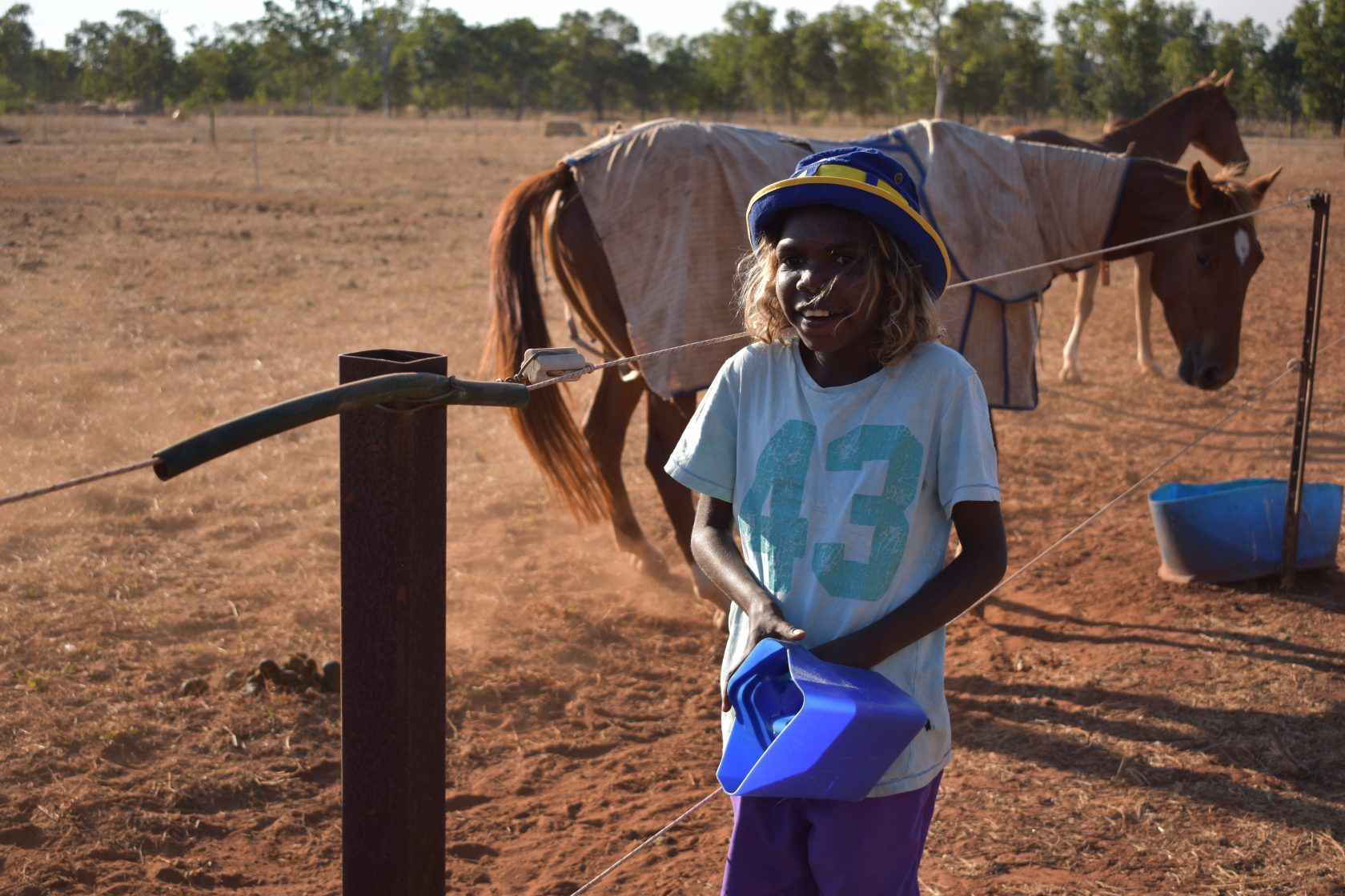 A young girl is standing in front of a horse holding a blue bucket.