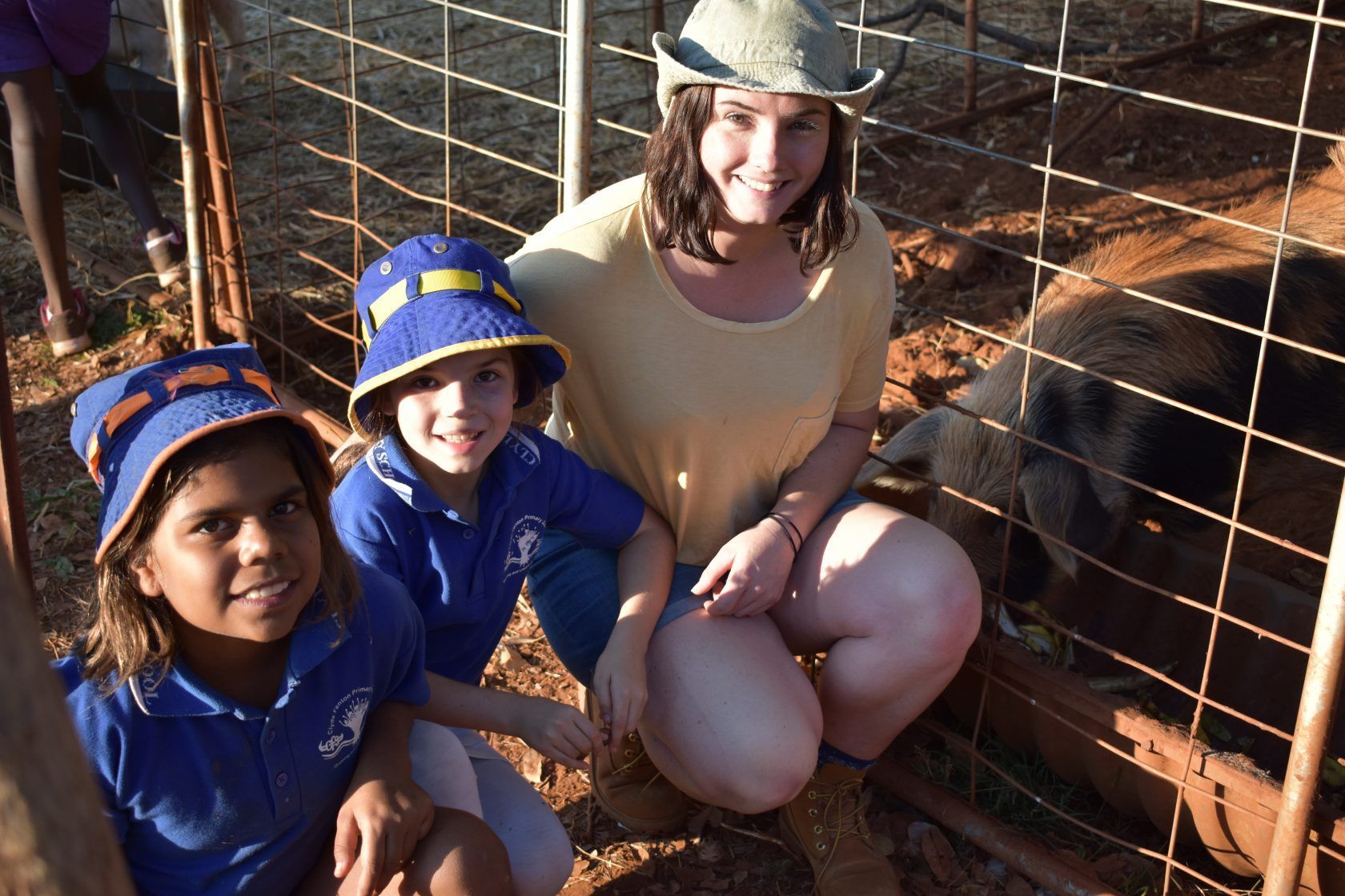 A woman is kneeling next to two children in front of a pig behind a fence.