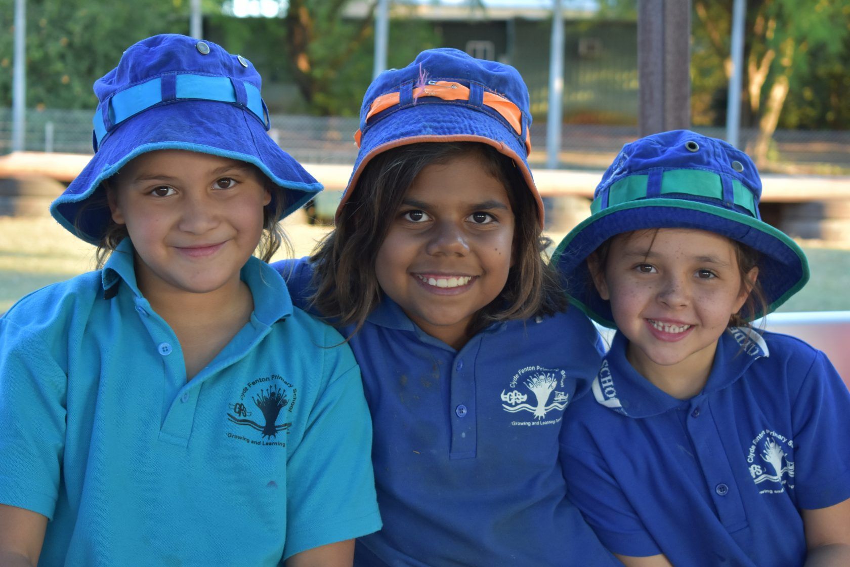 Three young girls wearing blue hats and blue shirts are posing for a picture.