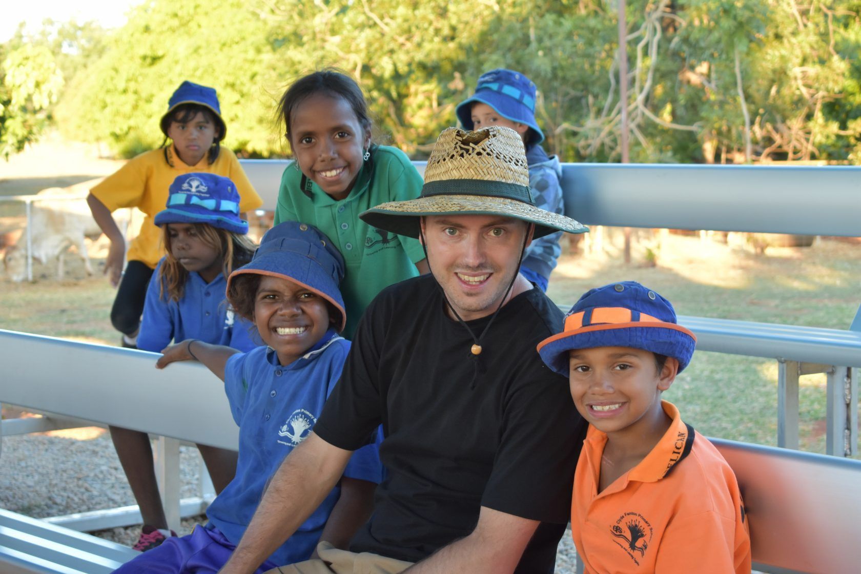 A group of children are posing for a picture with a man wearing a straw hat