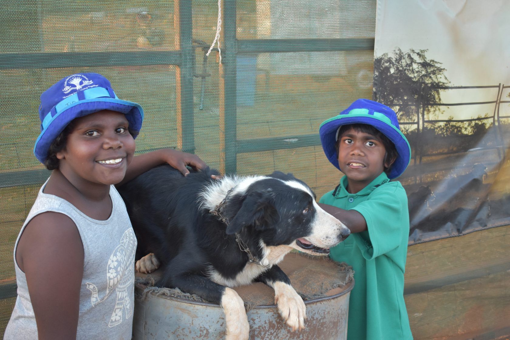 Two children petting a black and white dog wearing blue hats