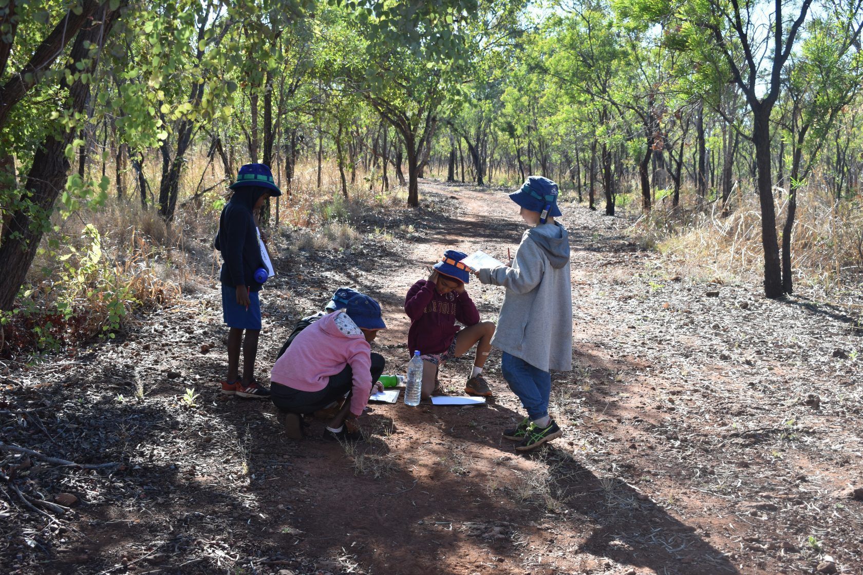 A group of children are standing on a dirt path in the woods.
