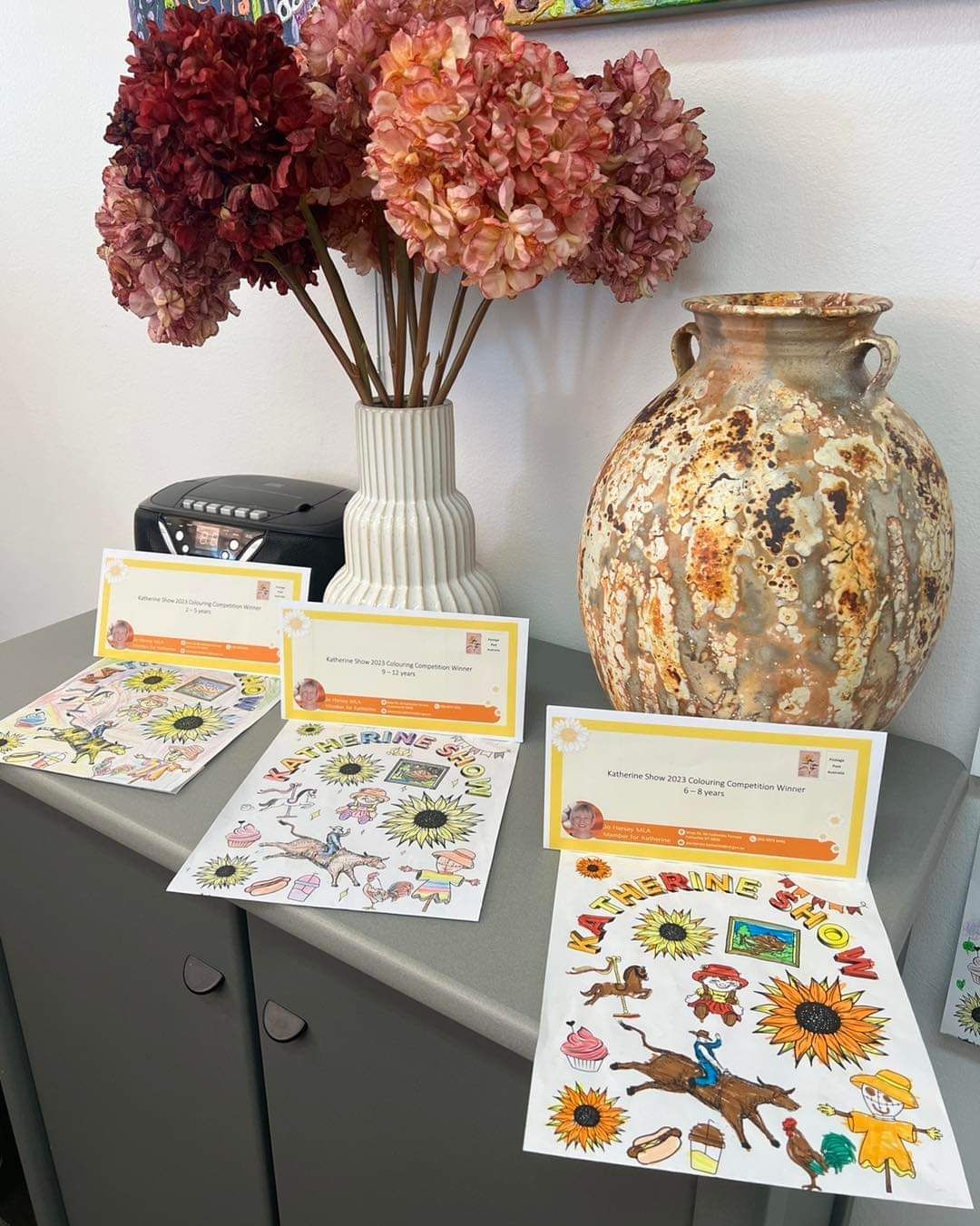 A vase of flowers is sitting on a table next to a vase of stickers.