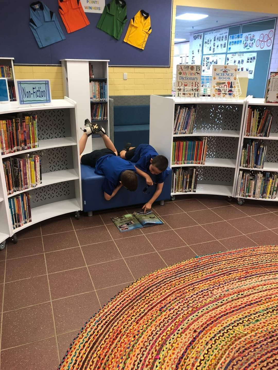 Two young boys are reading books in a library.