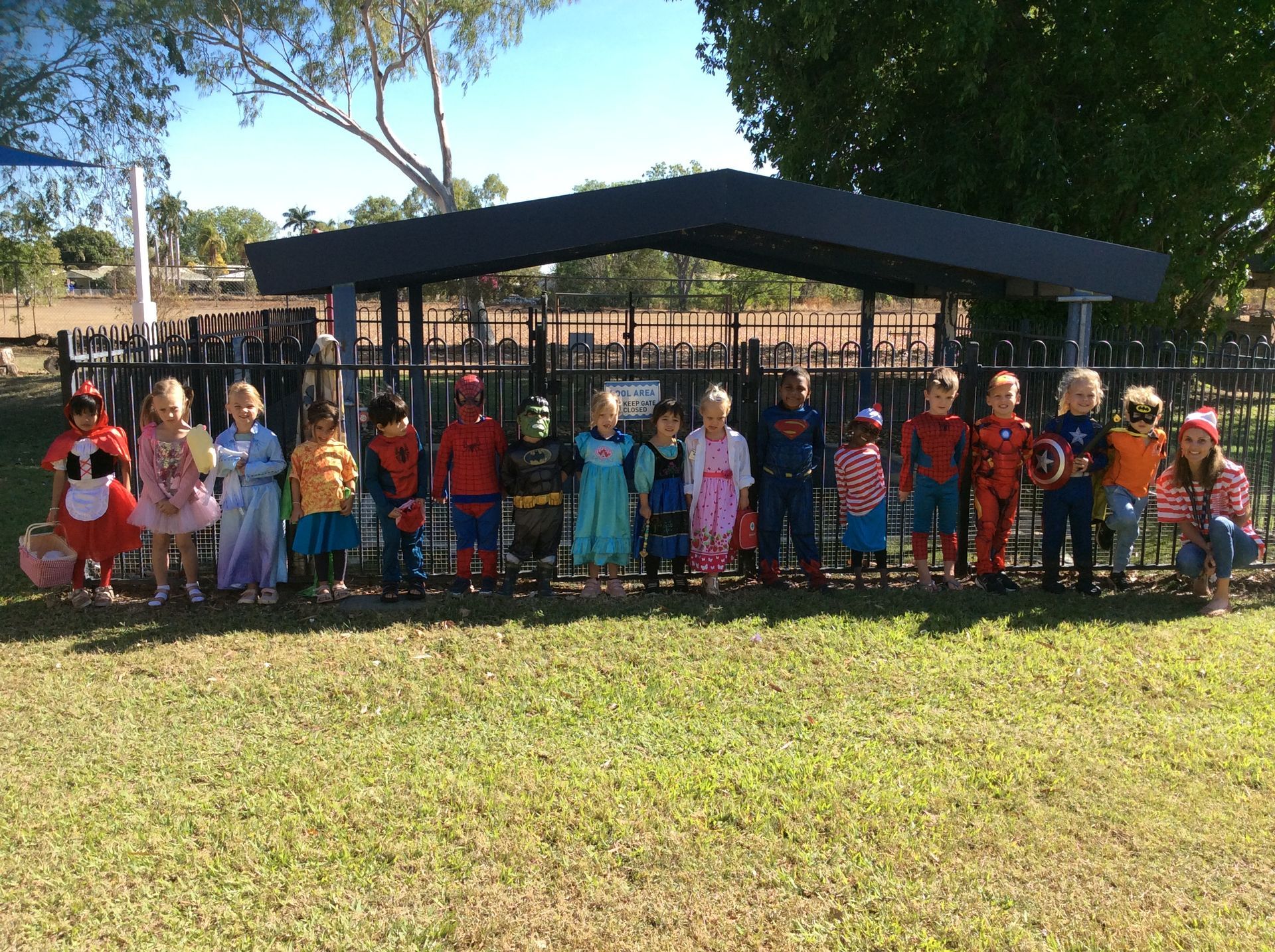 A group of children dressed in costumes are standing in a park.