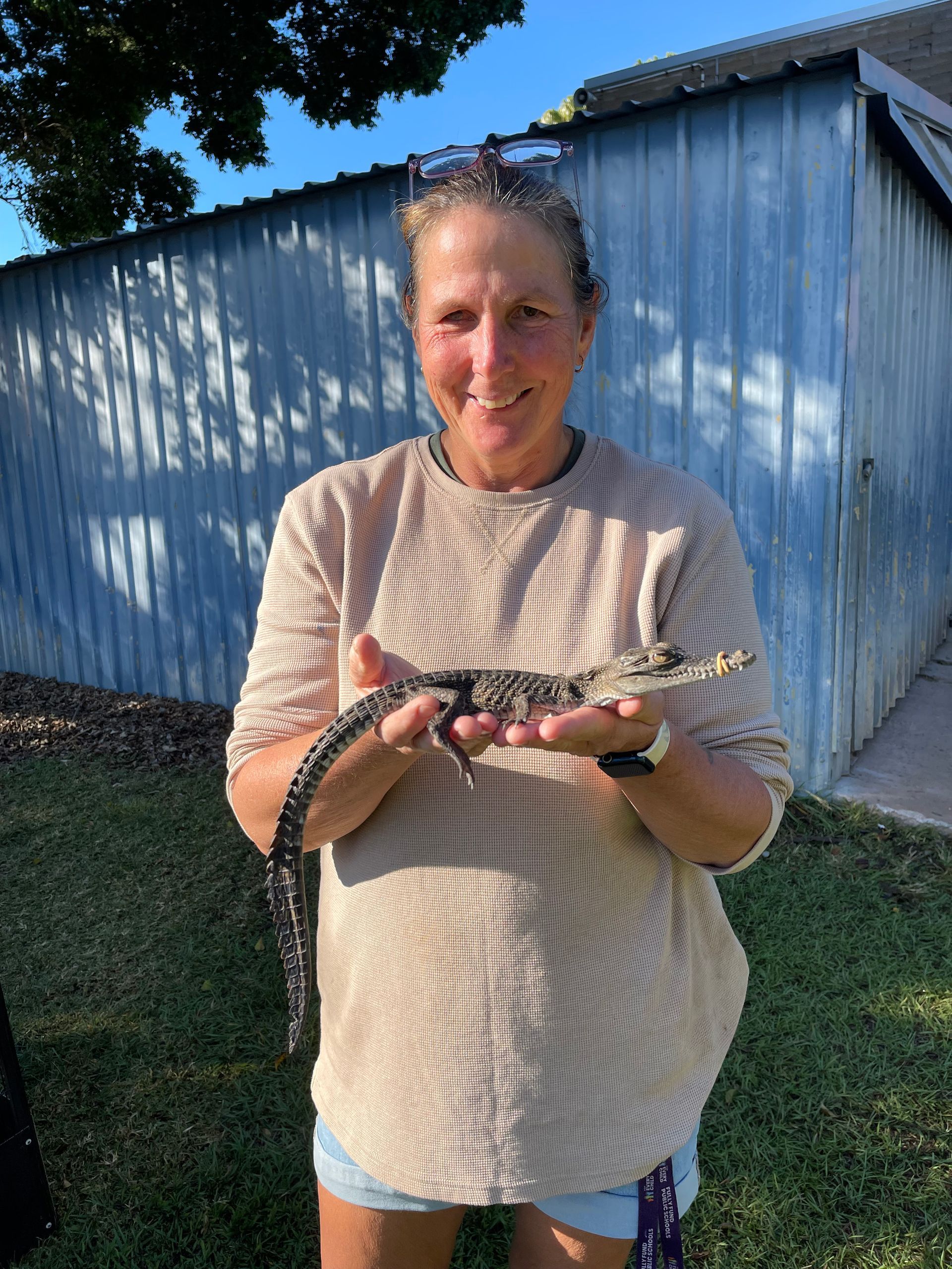 A woman is holding a small alligator in her hands.