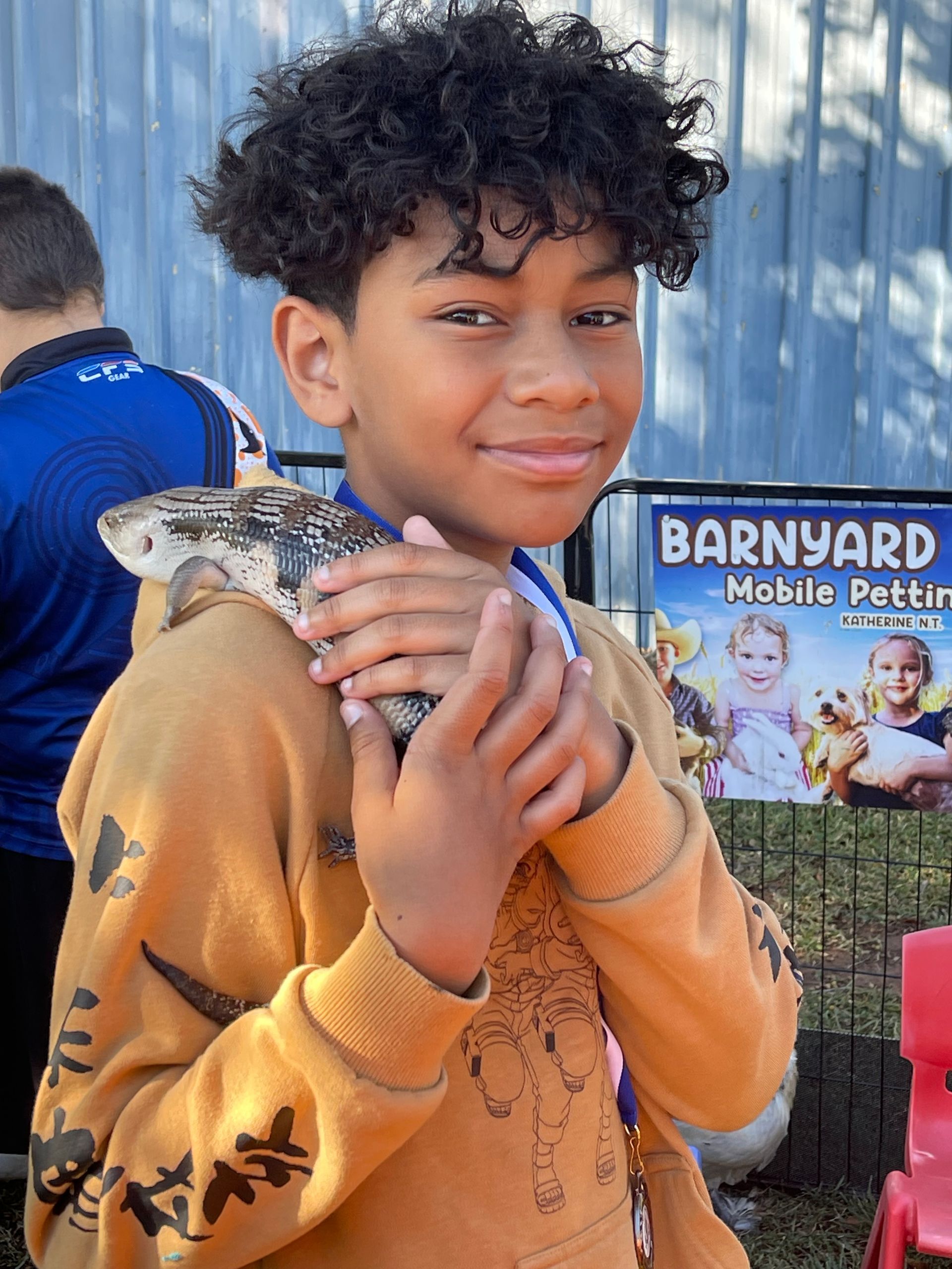 A young boy is holding a lizard on his shoulder.