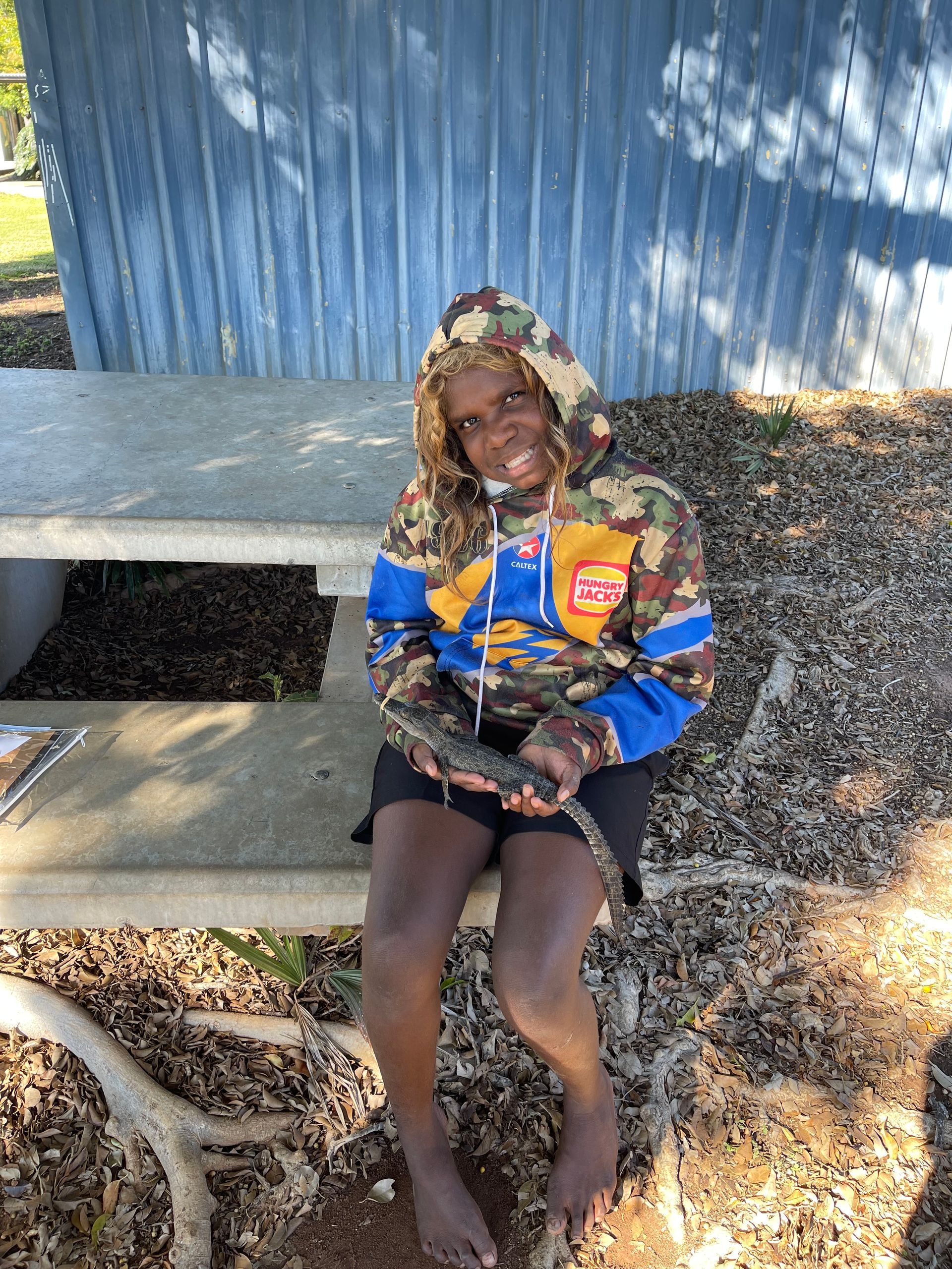 A young boy is sitting at a picnic table holding a snake.