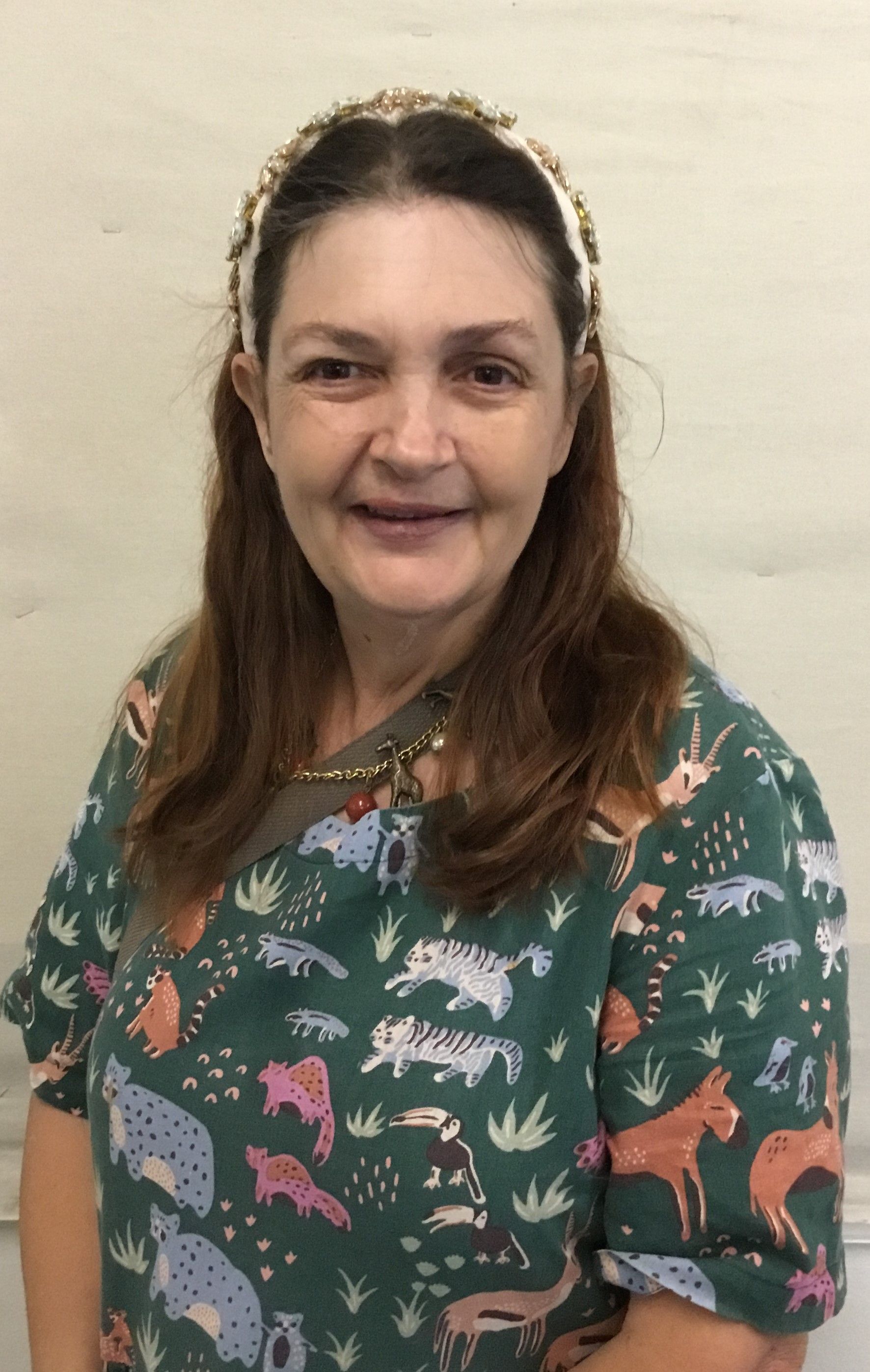 A woman wearing a green shirt with animals on it is smiling for the camera.