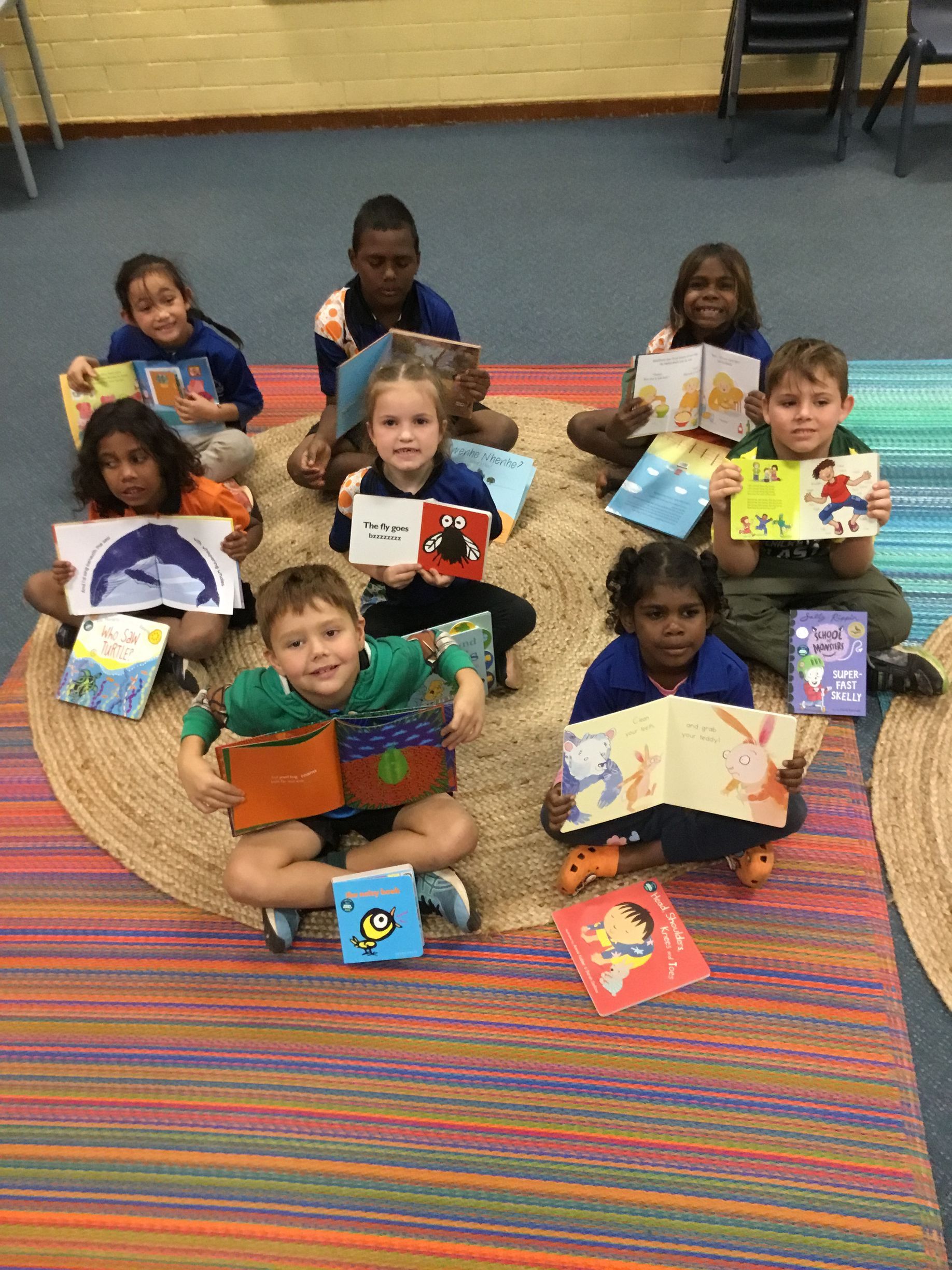 A group of children are sitting on the floor holding books.