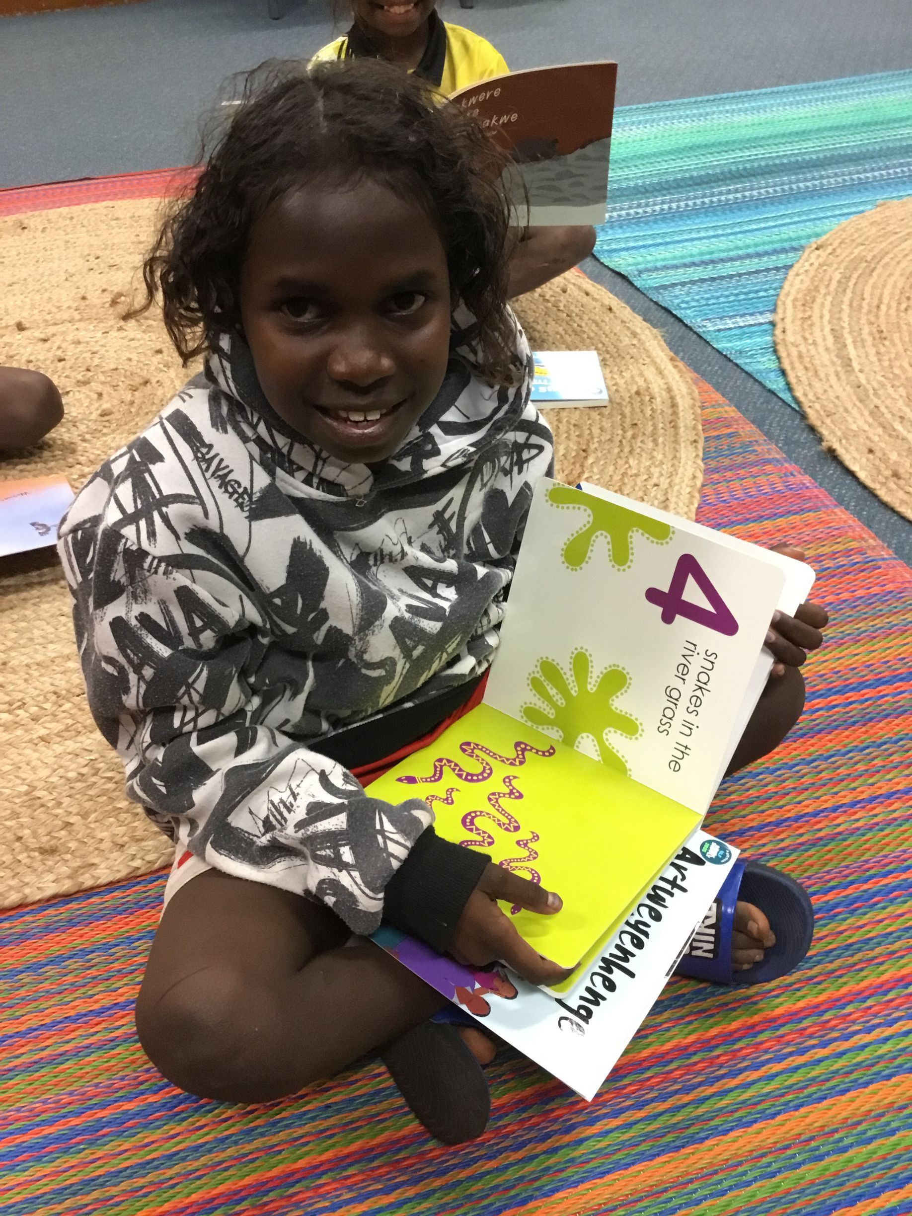 A young girl is sitting on the floor holding a book with the number four on it.