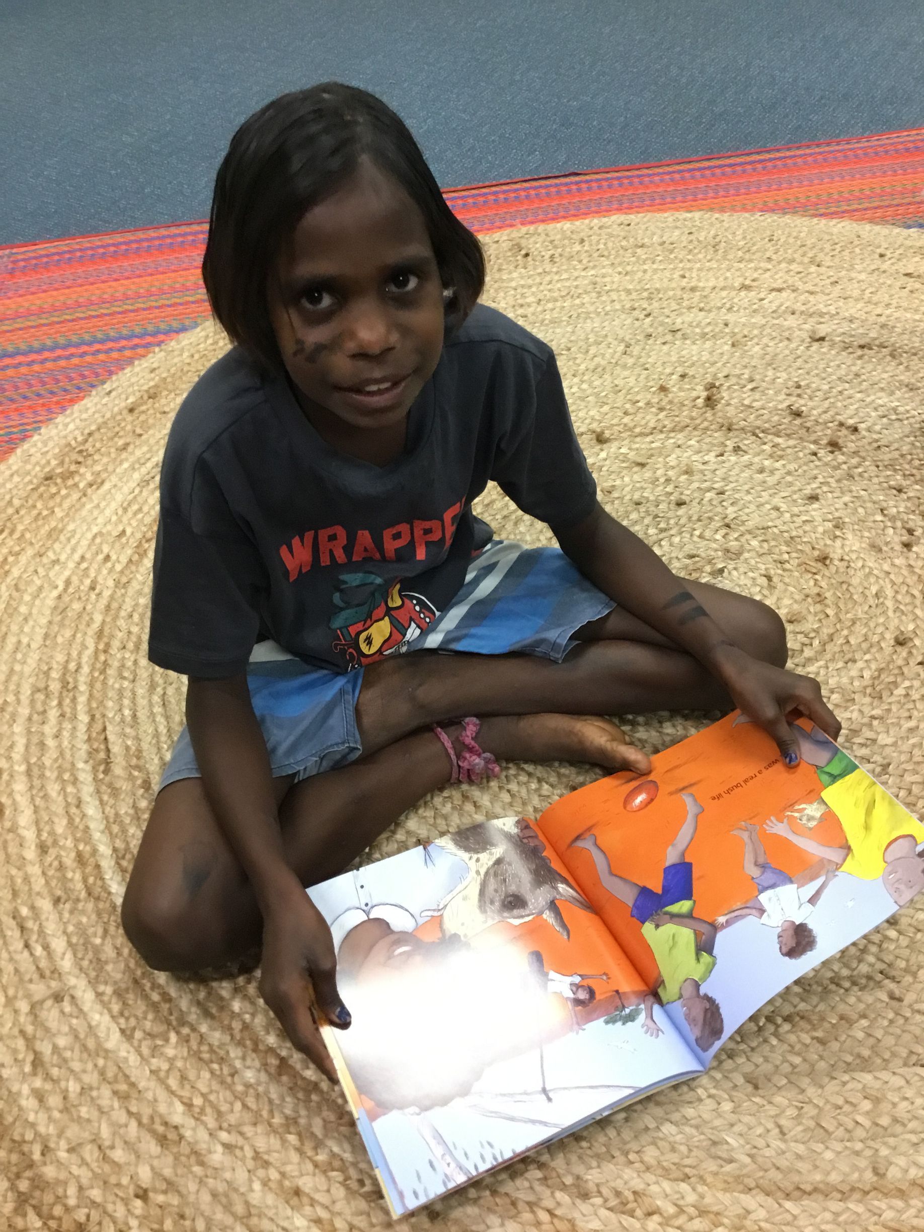 A young girl is sitting on the floor reading a book.