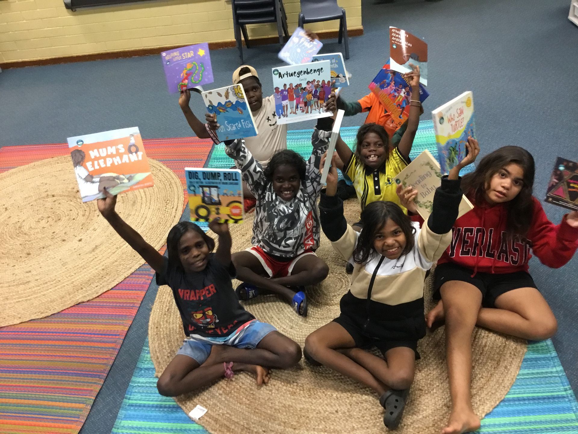 A group of children are sitting on the floor holding books in their hands.