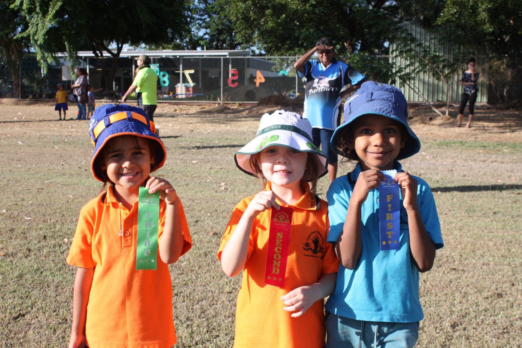 Three children wearing hats and holding ribbons in a field