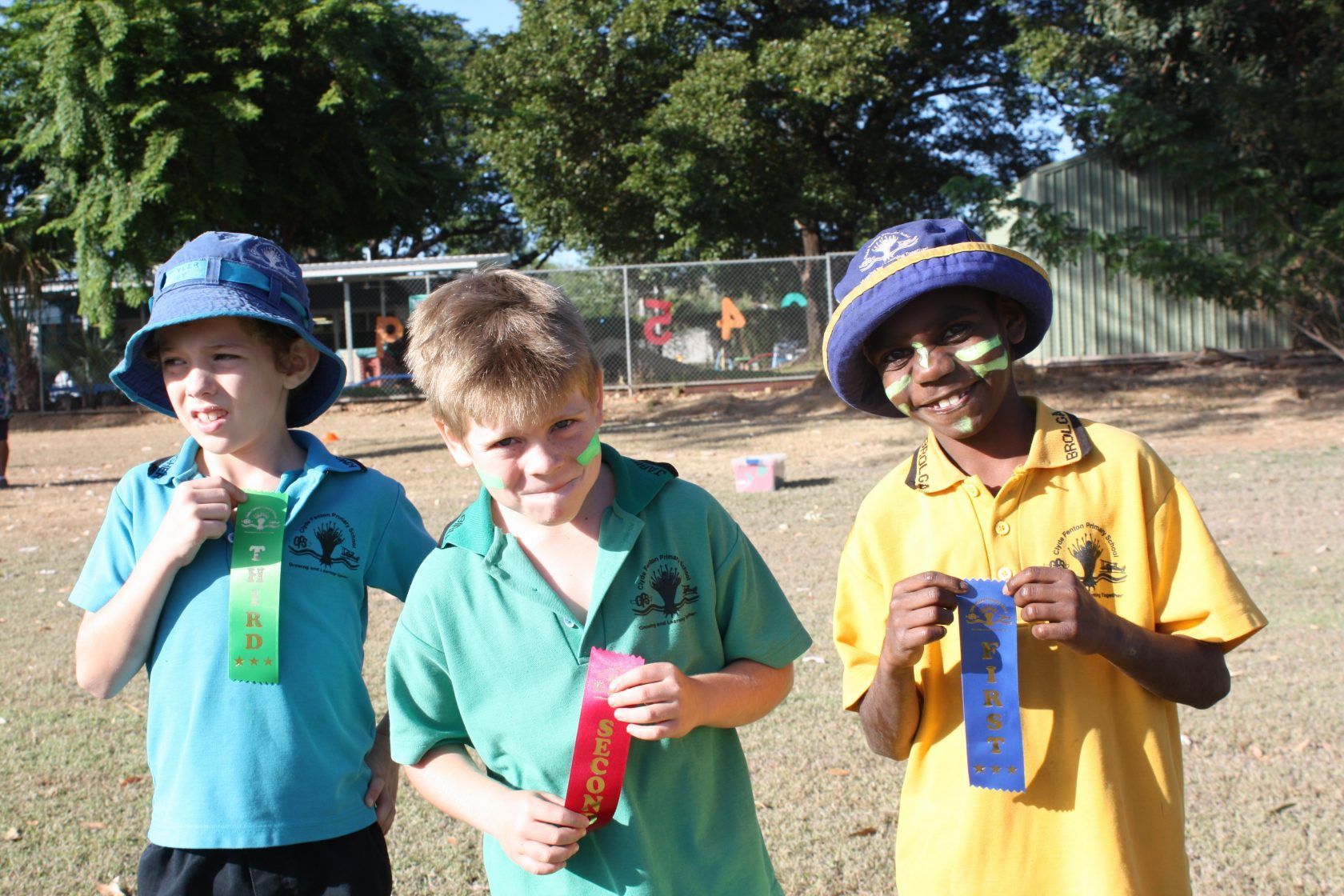 Three young boys are standing in a field holding ribbons