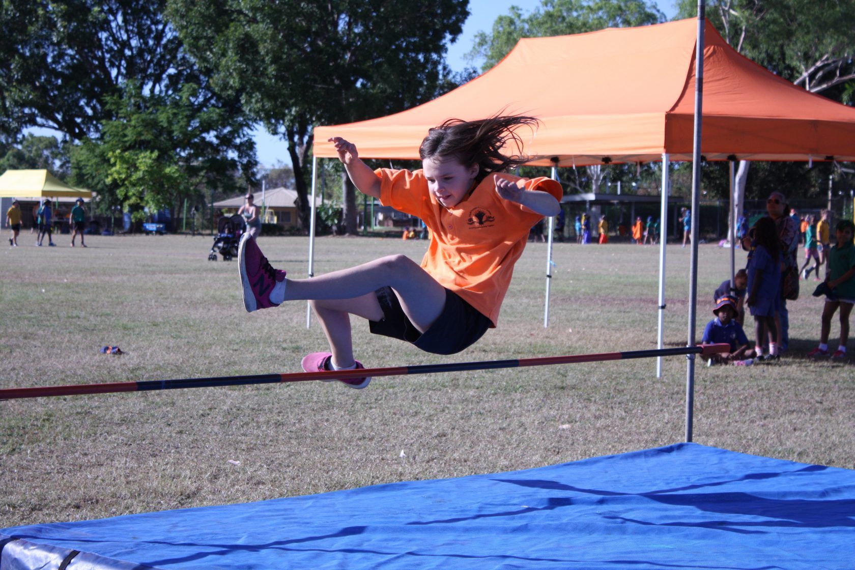 A girl in an orange shirt is jumping over a bar