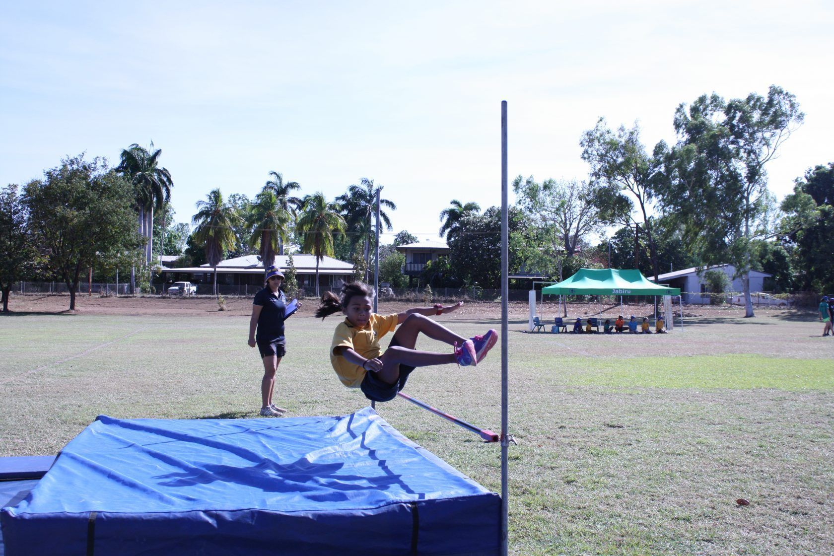 A girl is jumping over a pole in a field