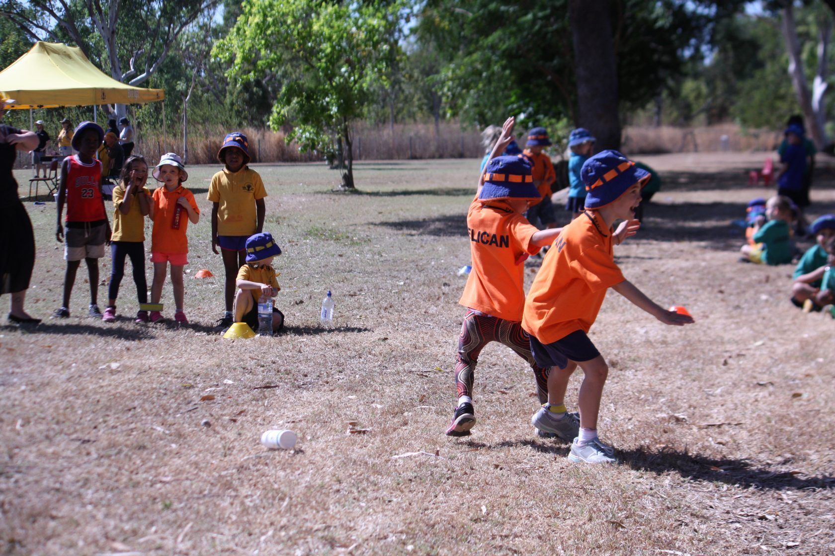 A group of children wearing orange shirts and hats are playing in a field