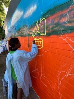 A young girl is painting a mural on a brick wall.