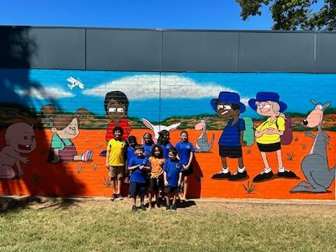 A group of children are posing in front of a mural of cartoon characters.