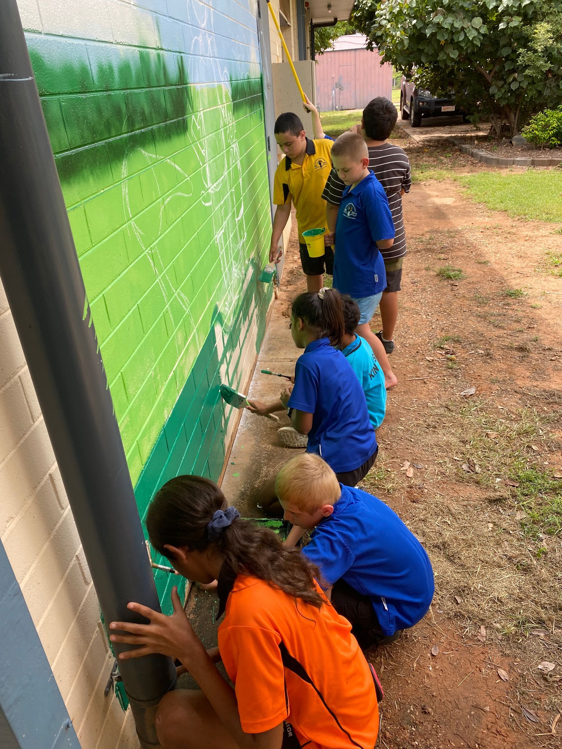 A group of children are painting a mural on a brick wall.