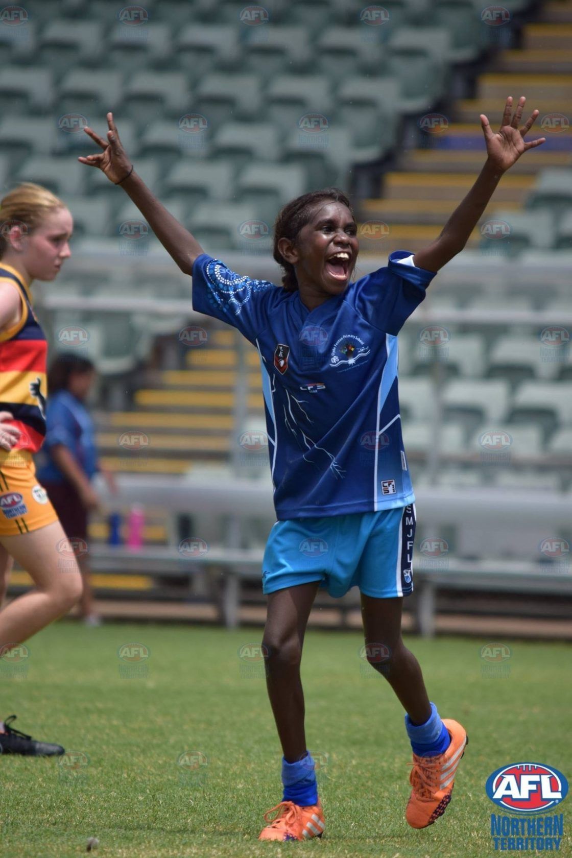 A young girl is playing soccer on a field with her arms in the air.