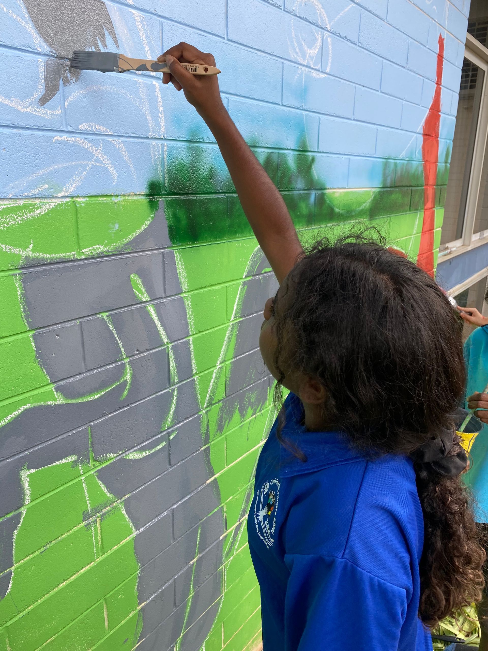 A young girl is painting a mural on a brick wall.