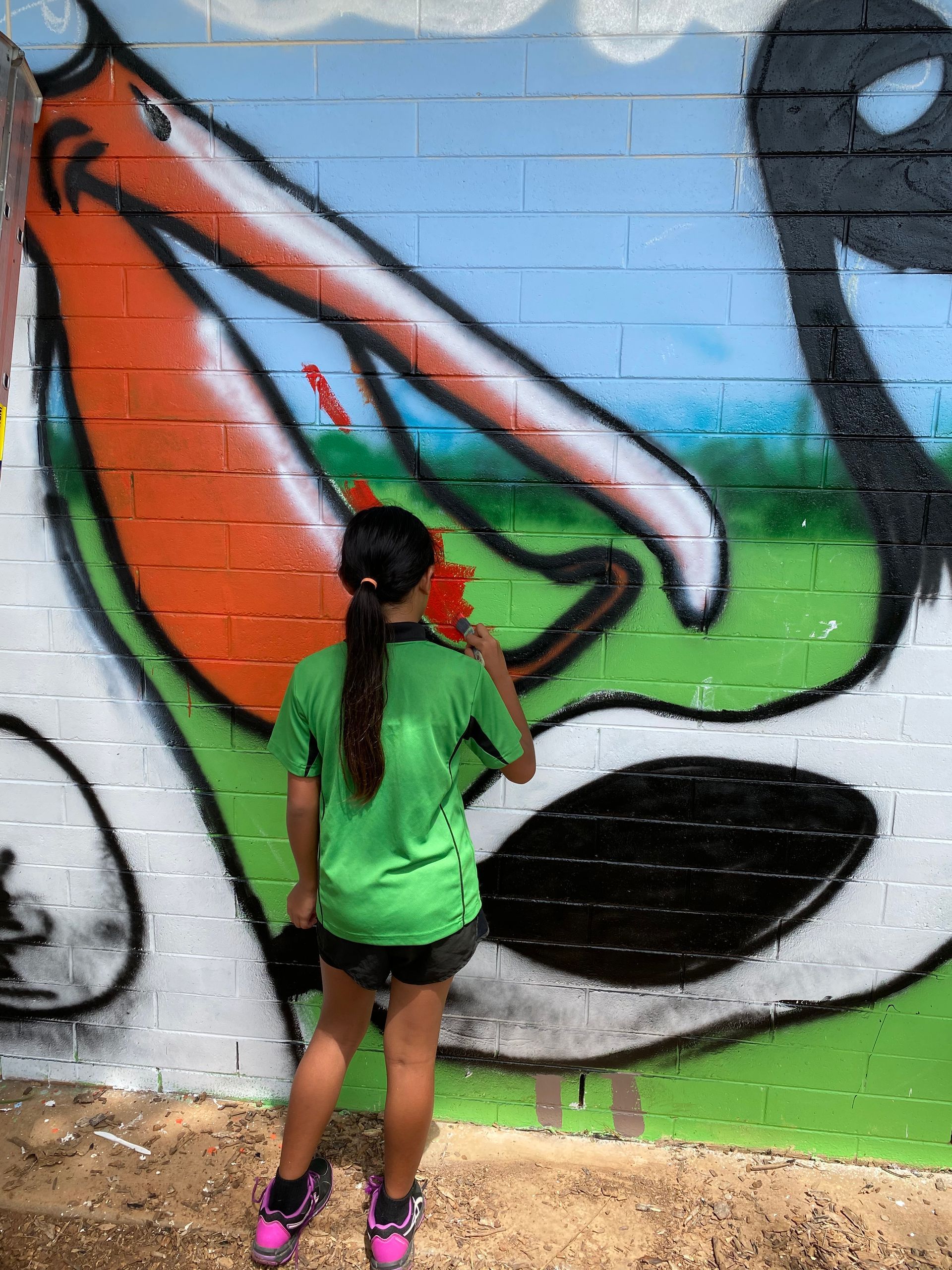 A girl in a green shirt is standing in front of a mural of a pelican