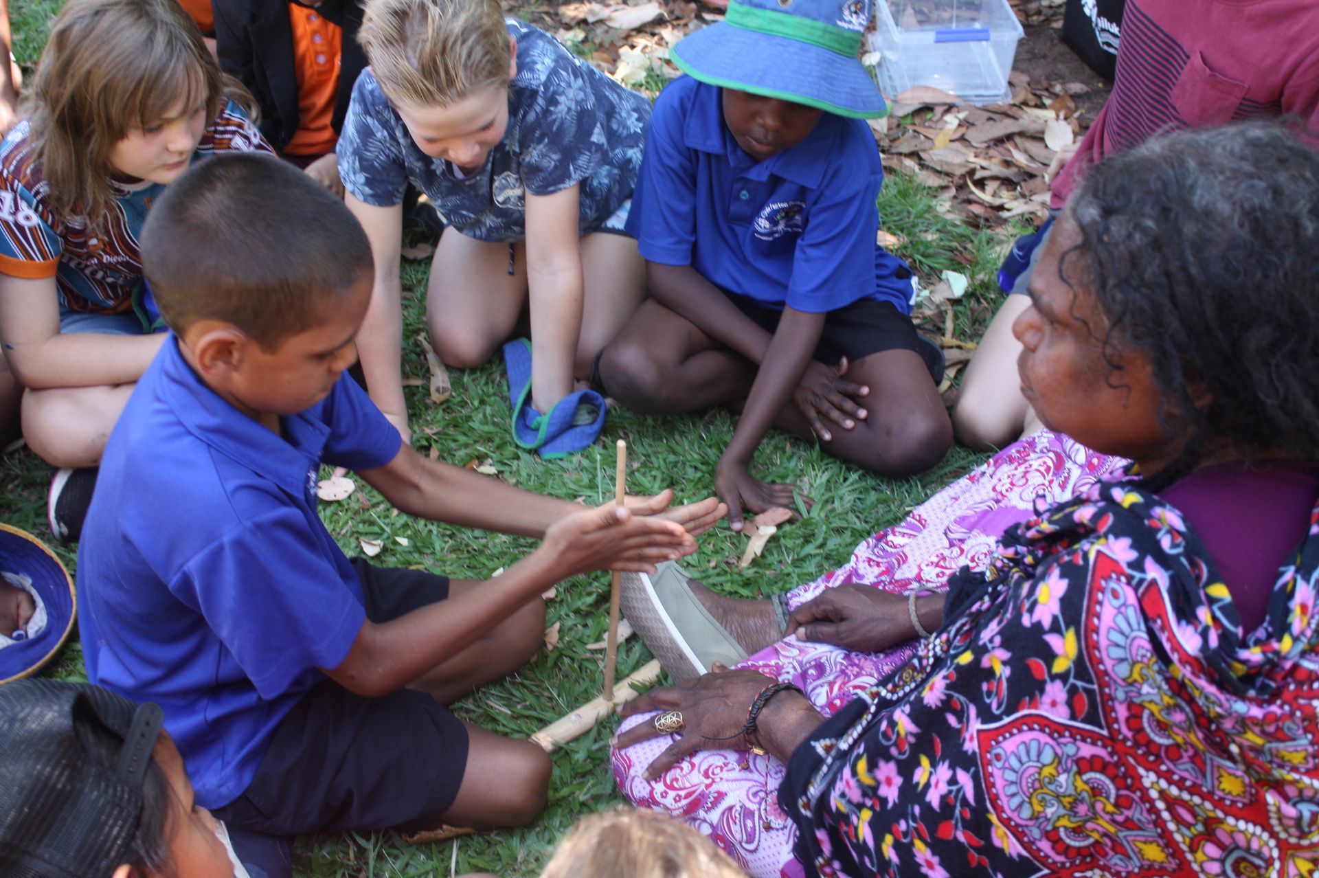 A group of children are sitting in a circle on the grass with a woman.