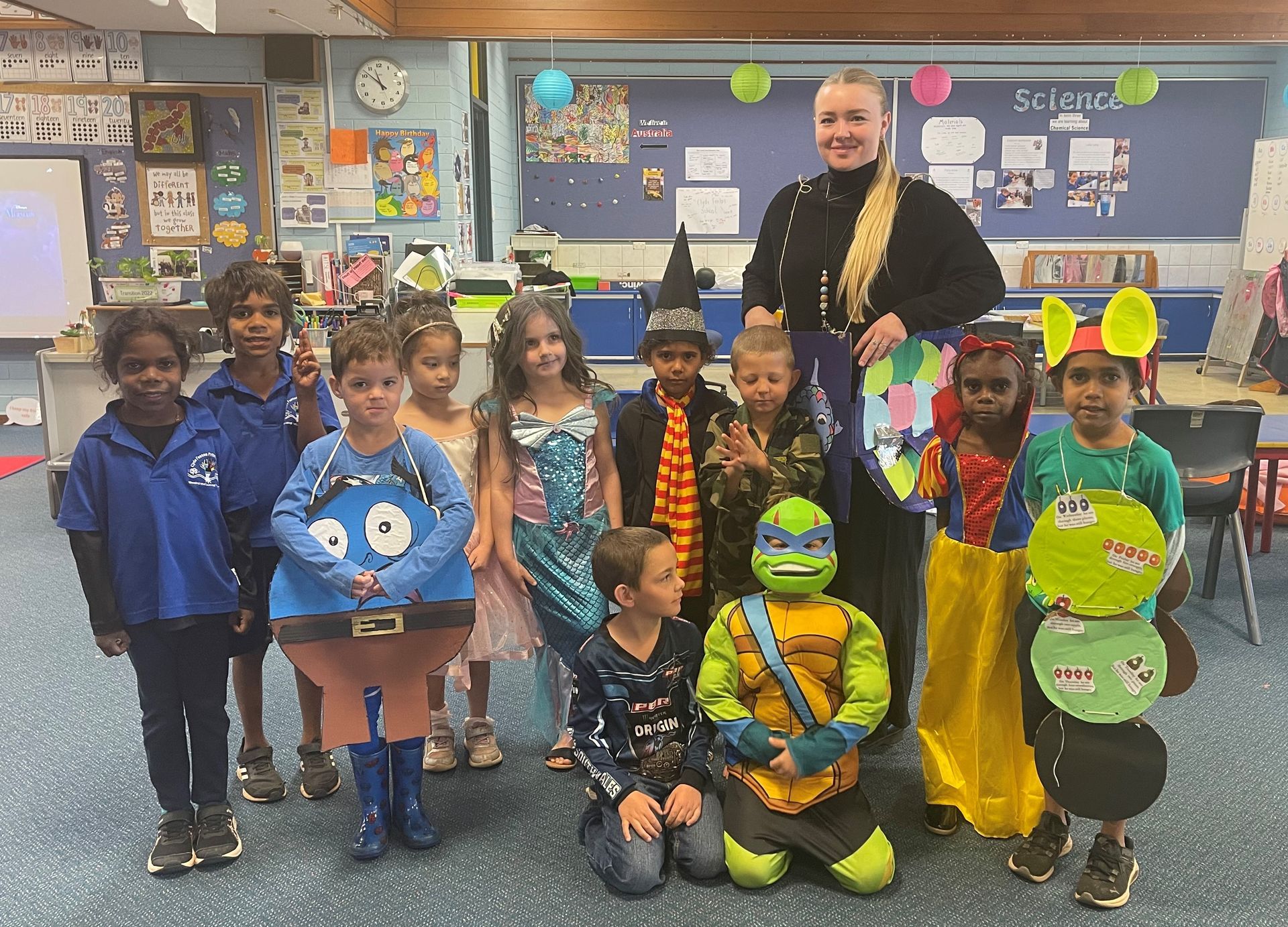 A group of children in costumes are posing for a picture in a classroom.