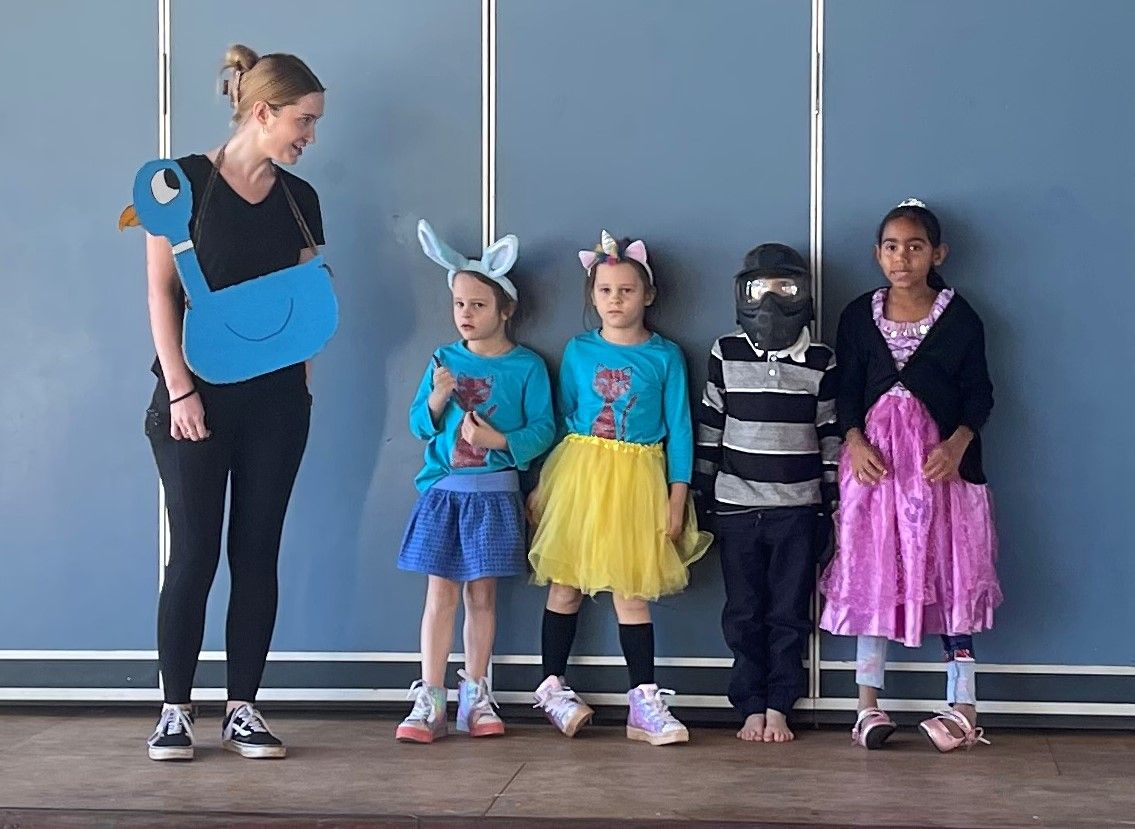 A woman is standing next to a group of children dressed in costumes.