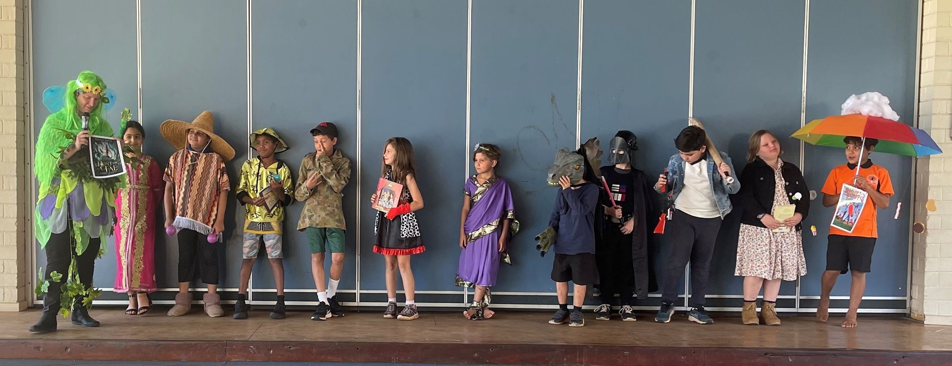 A group of children dressed in costumes are standing in front of a wall.