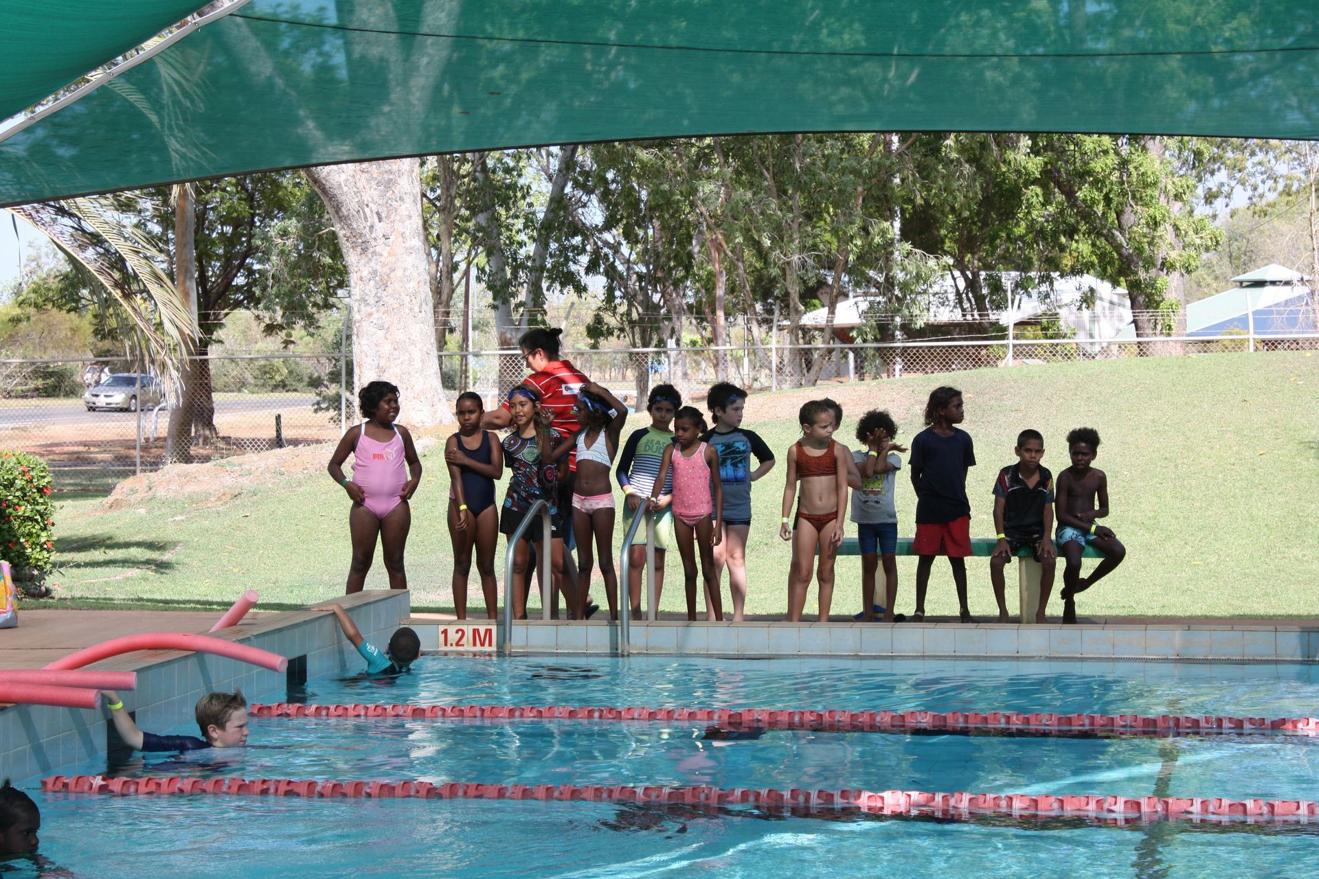 A group of children are standing next to a swimming pool.