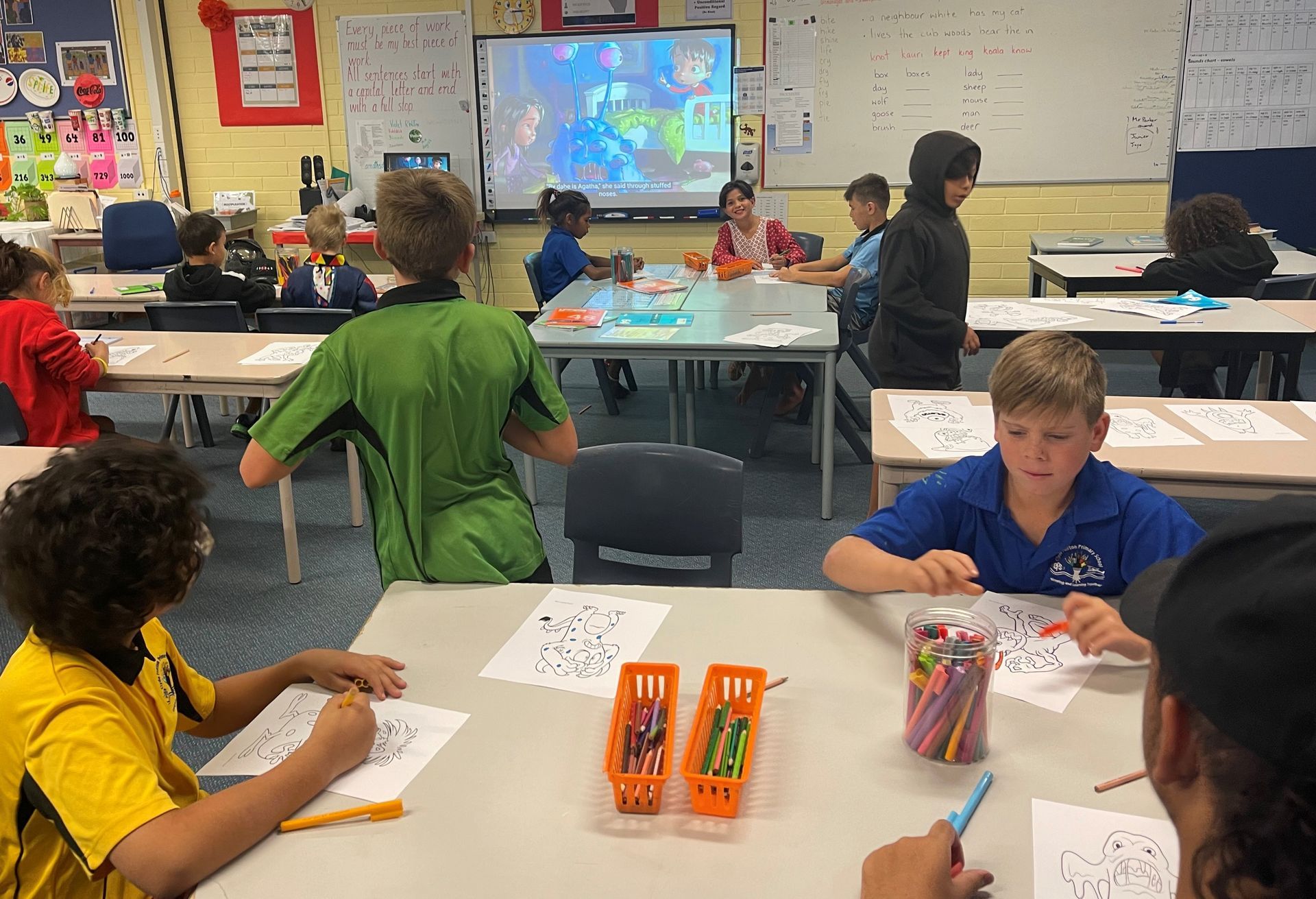 A group of children are sitting at tables in a classroom.