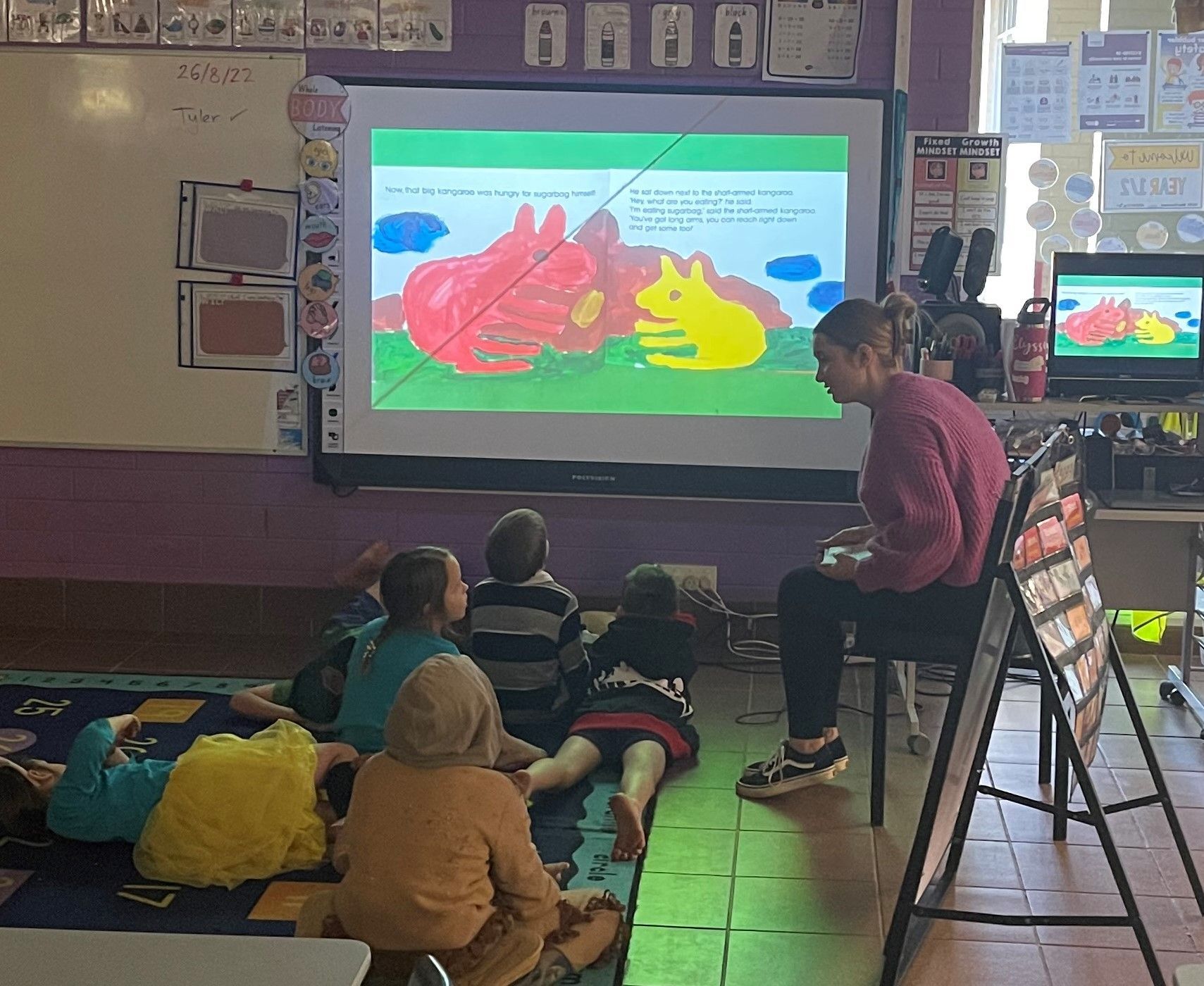 A group of children are sitting on the floor in front of a projector screen