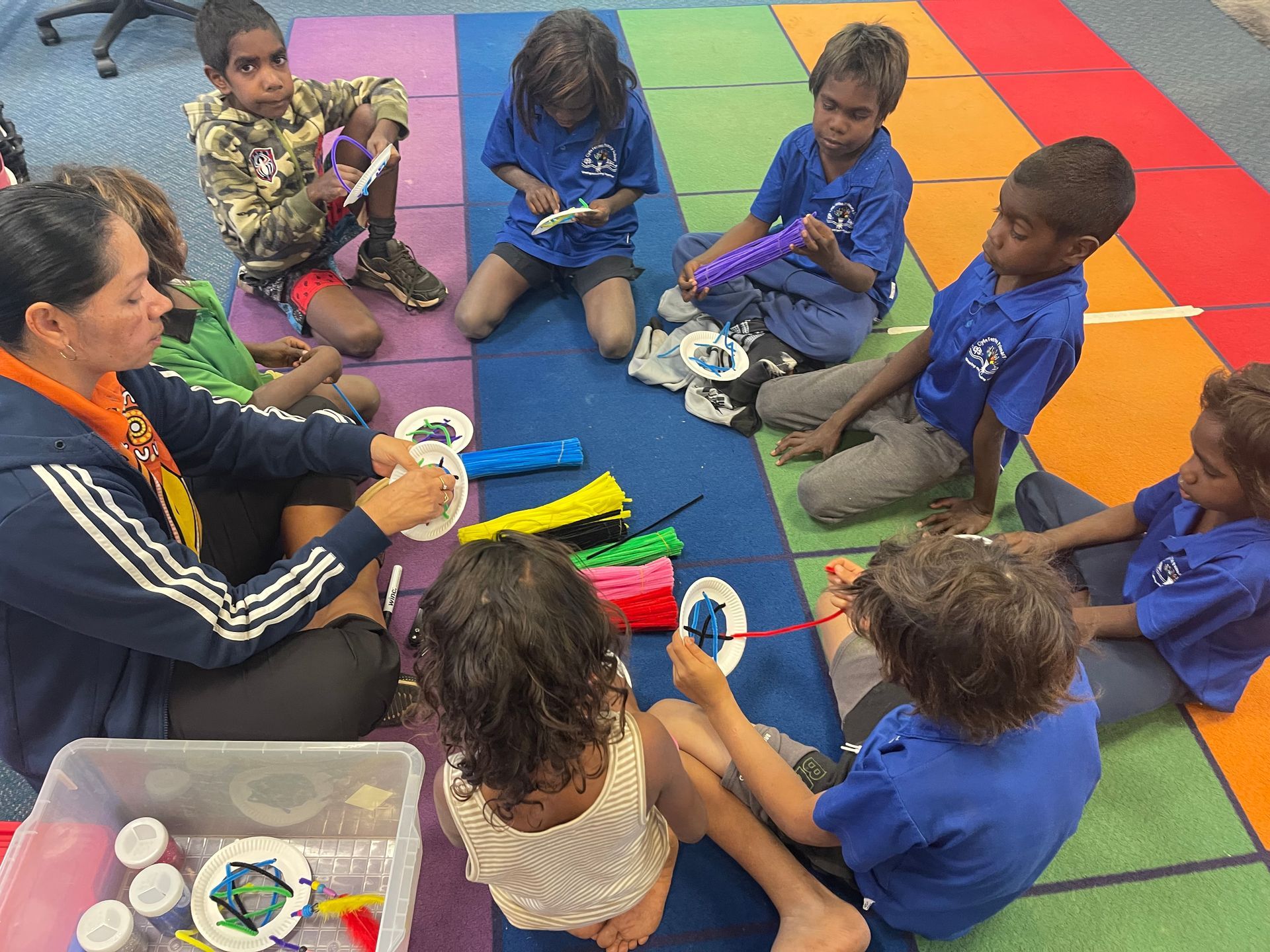 A group of children are sitting on the floor with a teacher.