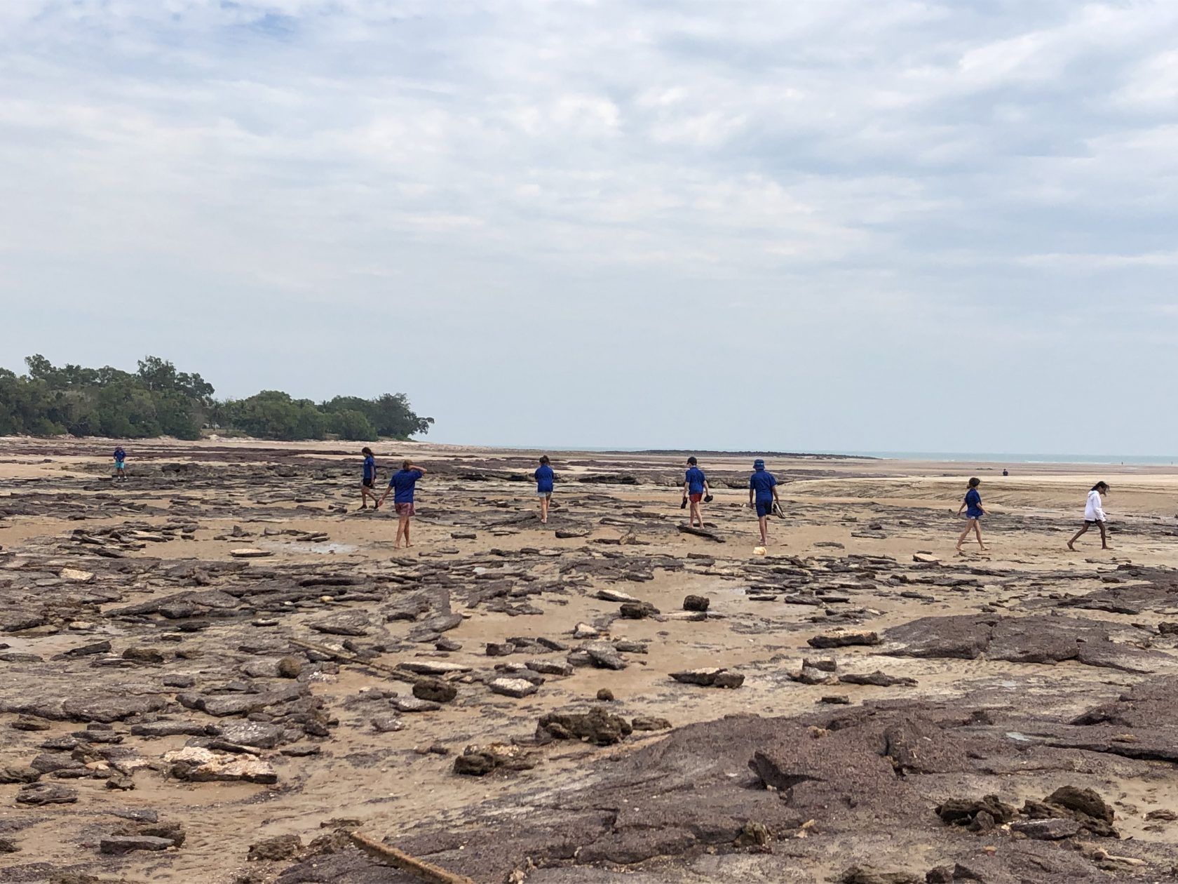 A group of people are walking on a rocky beach.