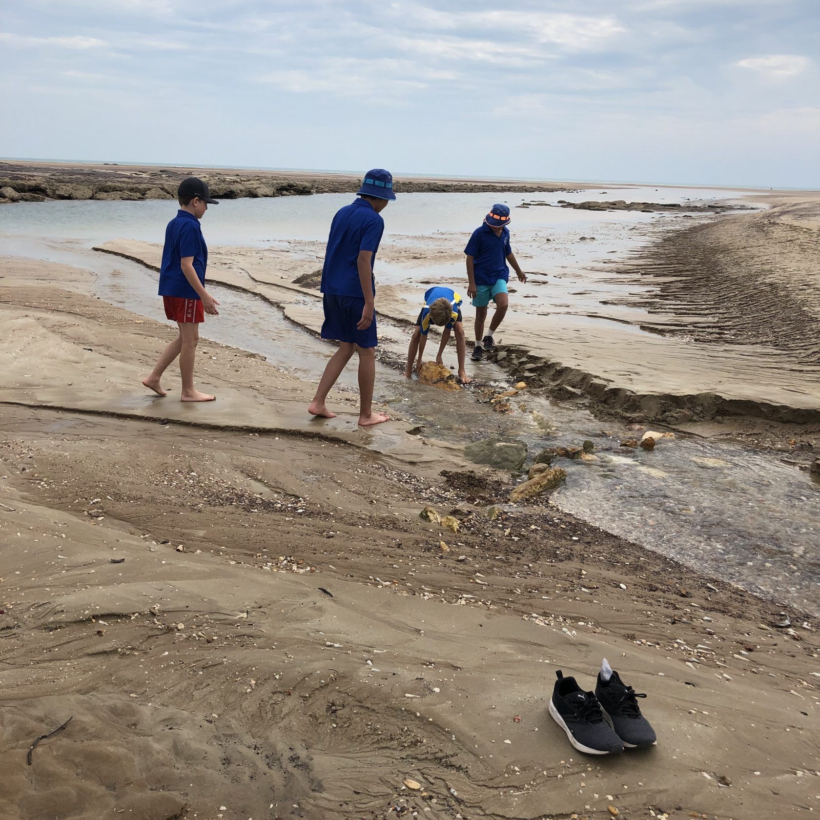 A group of people walking on a beach near a stream