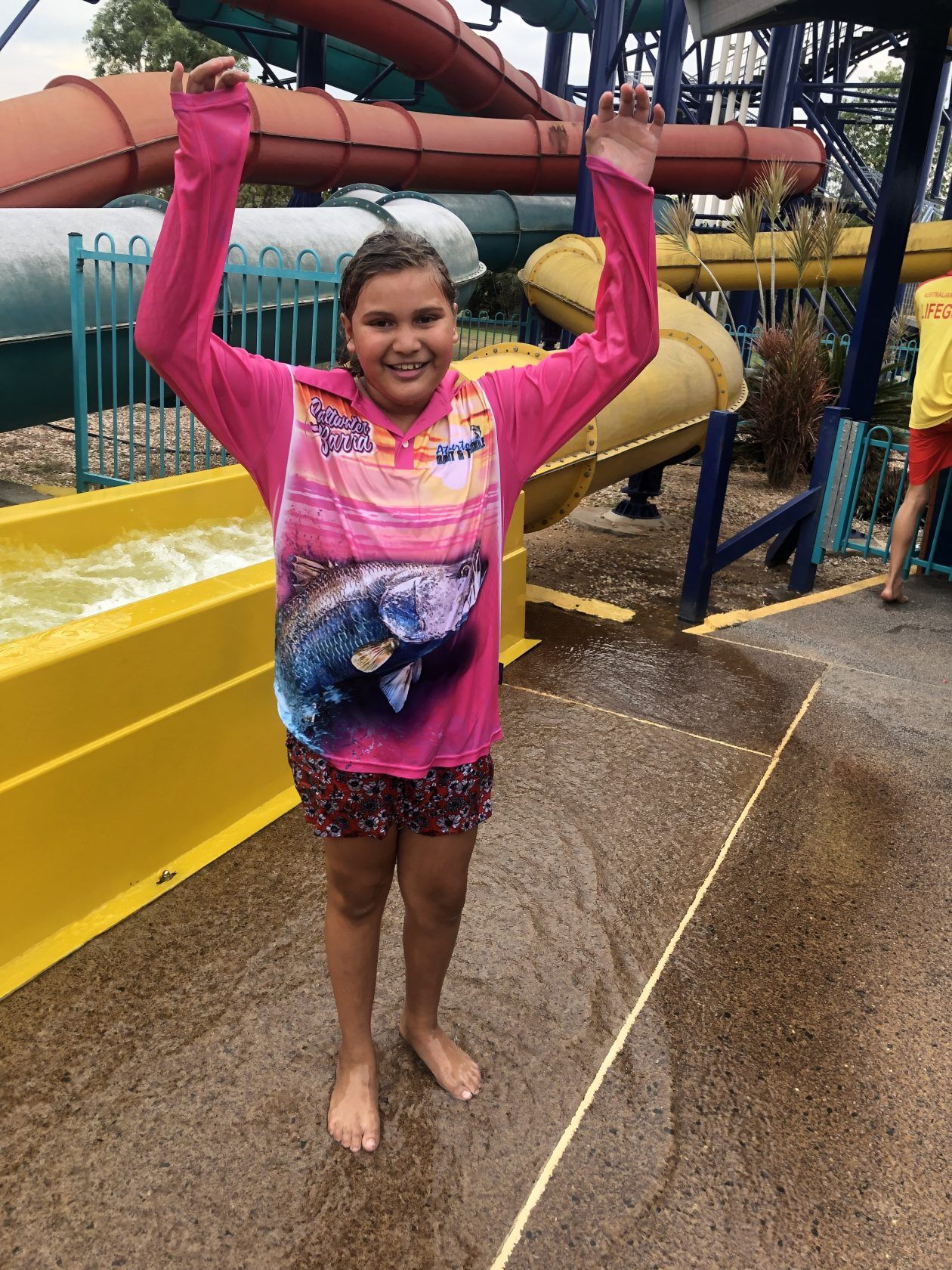 A young girl is standing in front of a water slide at a water park.