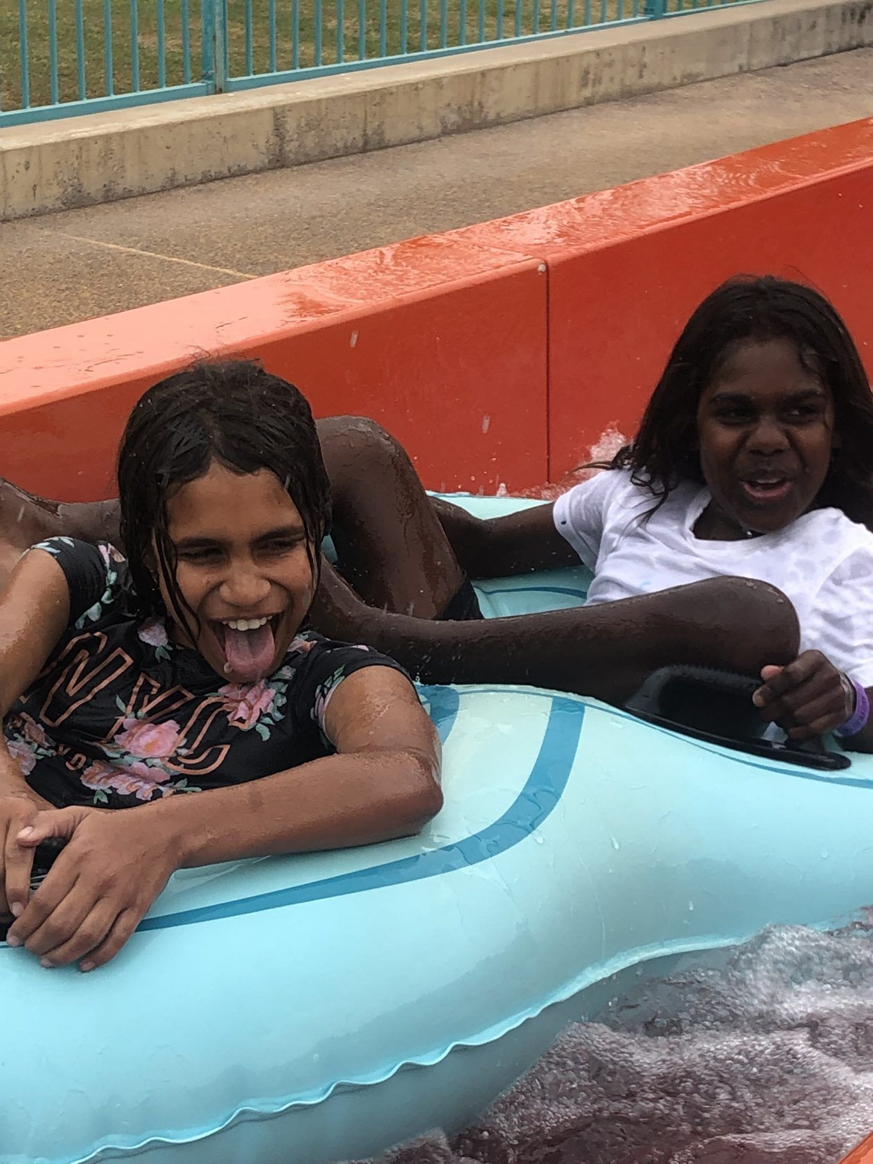 Two young girls are riding a water slide at a water park.