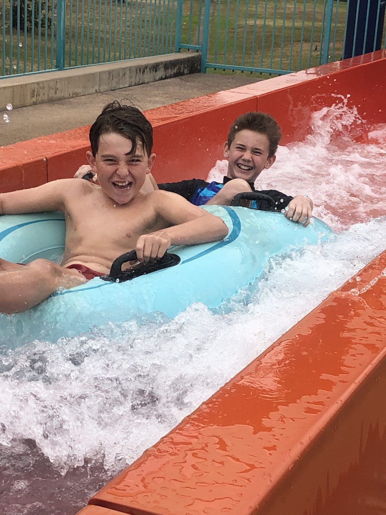 Two young boys are riding a water slide at a water park.