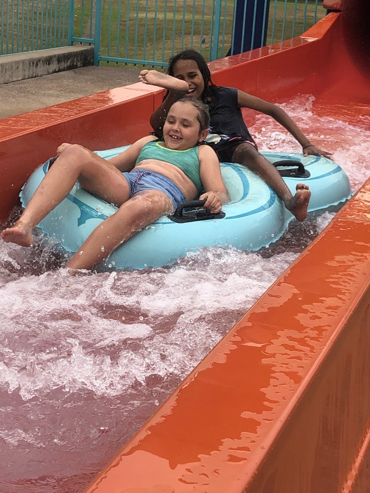 Two young girls are riding down a water slide on a tube.